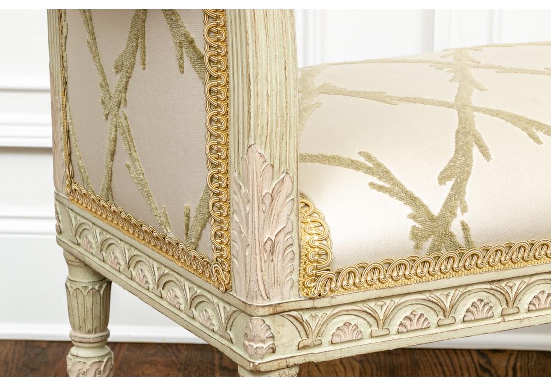 Fine construction with elegant carved frame in greenish cream paint- scrolled arms with leafy ends, cylindrical fluted tapering legs with leafy tops, the skirt rail with arches and palmettes. Upholstered in custom cut velvet in a sage green