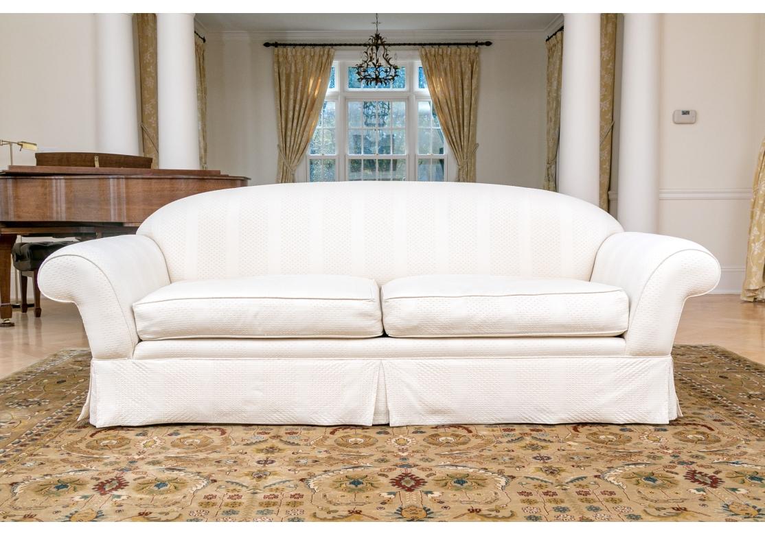 A very beautifully upholstered curve back sofa with wide flat panel arms, skirted with four custom  toss pillows. The fabric is a deceptively simple yet intricate quilted type with tiny repeating geometric honeycombed motif. Very well made and quite