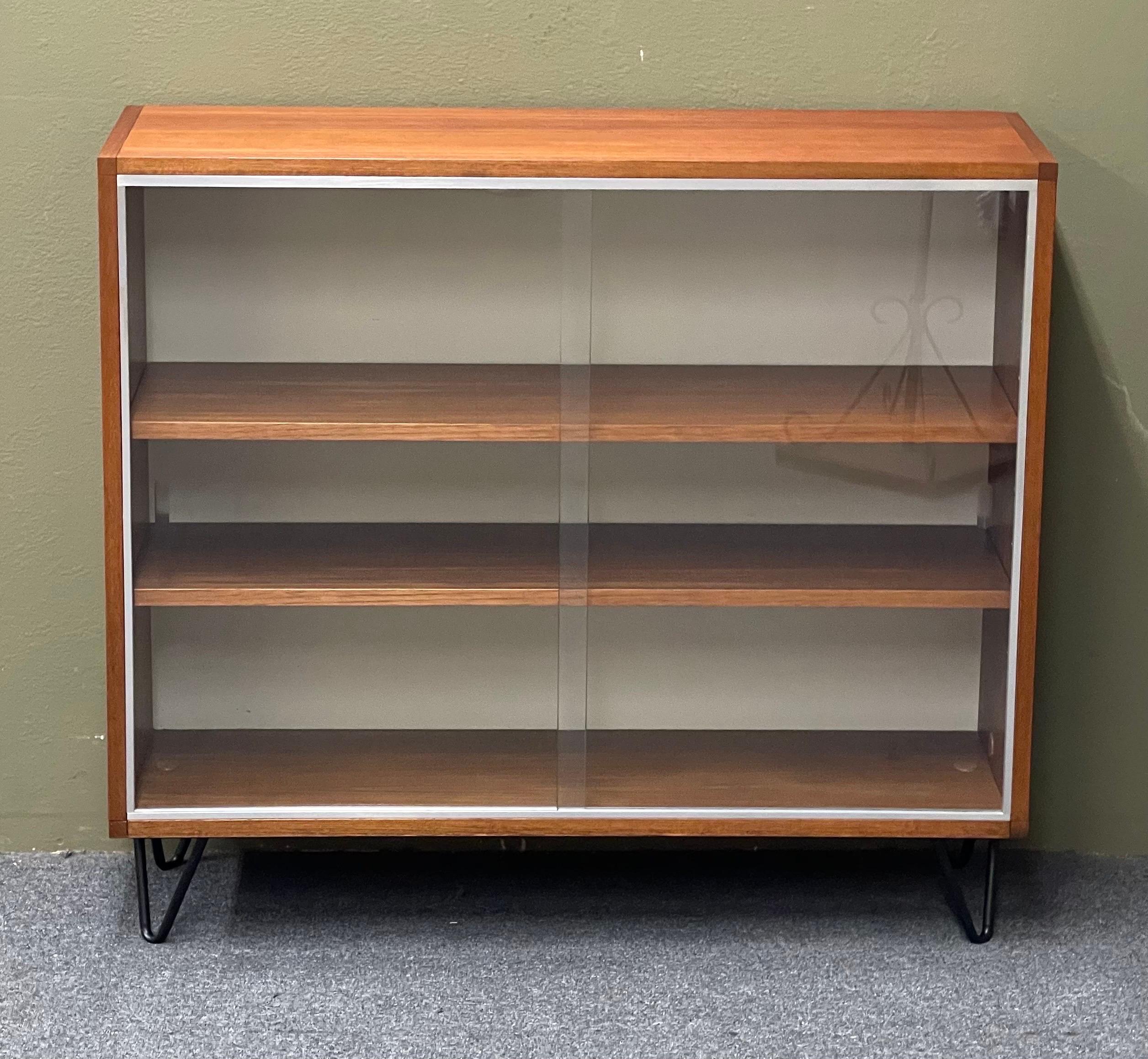 Beautiful and elegant Danish modern bookcase / cabinet, circa 1960s. The bookcase is in very good vintage condition and has been professionally refinished. It has adjustable shelves, two sliding glass doors, hairpin legs and a white board back. The