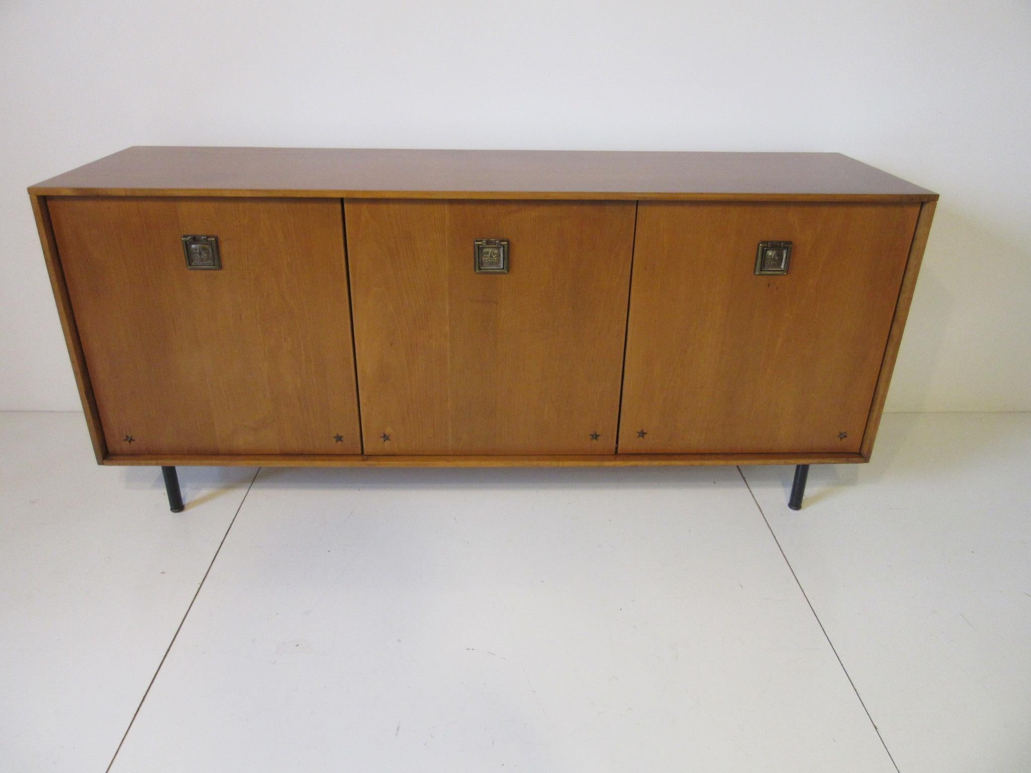 A three door solid maple credenza with drawers to the middle, fronts in satin black as well as the adjustable shelves to each ends and having a finished backside. Sitting on satin black steel legs with brass ornamental pulls and details in the