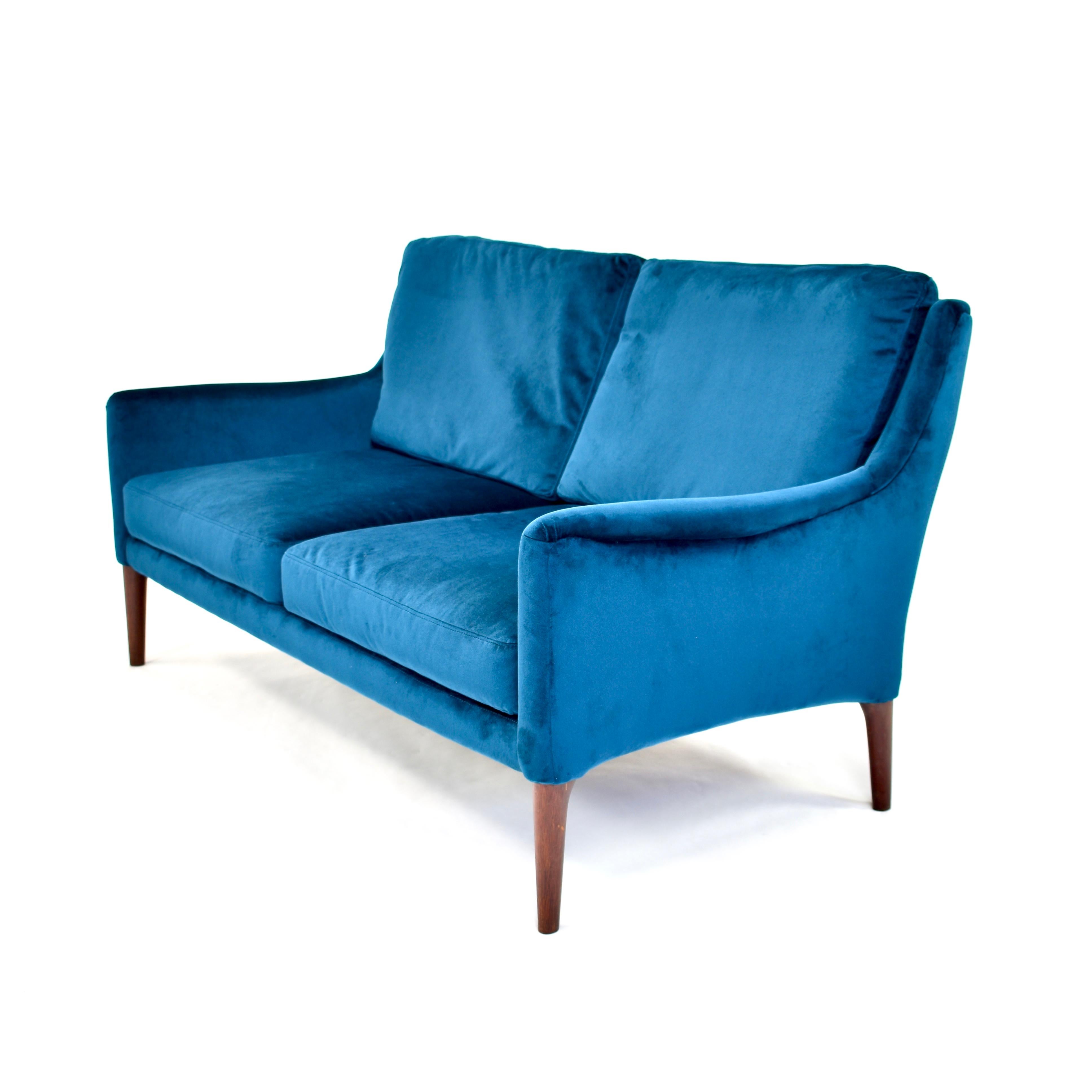 Elegant Danish two-seat sofa in beautiful Emerald green velvet fabric and solid teak legs. (In the pictures the fabric appears to be blue but it is emerald green).
The sofa is very comfortable and soft to sit in. Feather filling in the