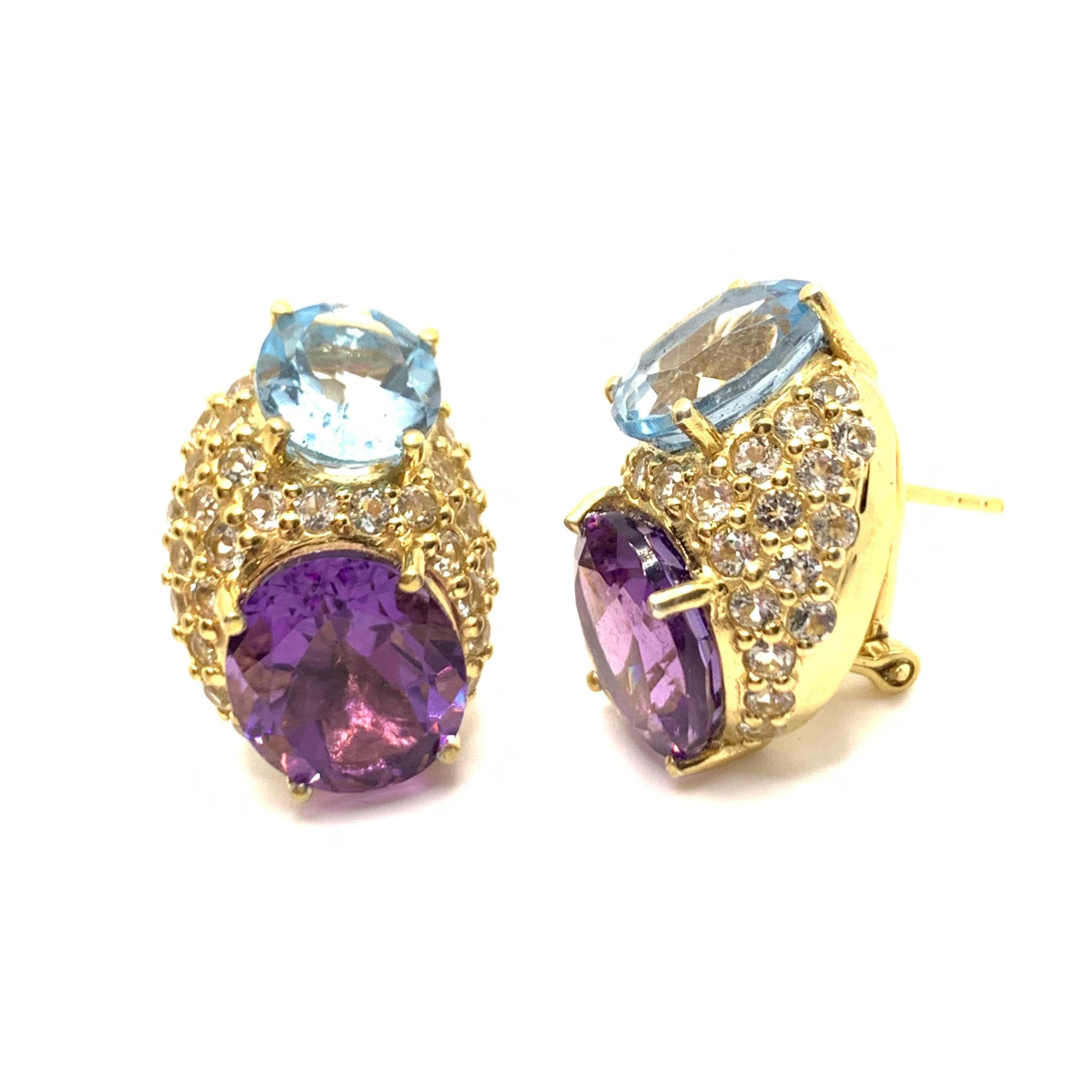 These stunning pair of earrings features a set of genuine sky blue topaz and Brazilian purple amethyst, adorned with 54 pieces of round white topaz, handset in 18k yellow gold vermeil over sterling silver. The facets from the oval stones together