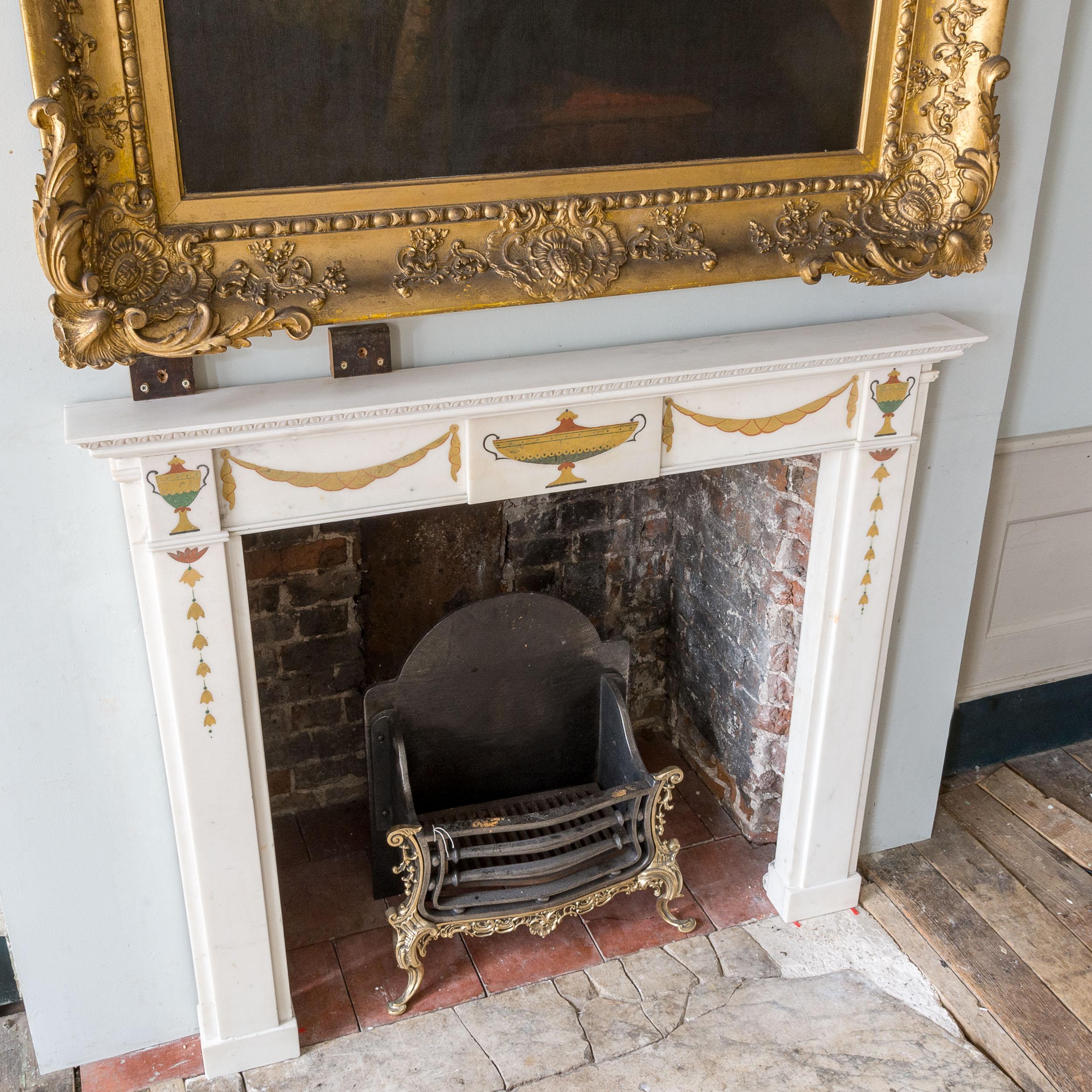 Elegant early twentieth century Statuary marble neo-classical fire surround, in the Regency manner, the lambrequin moulded rectangular shelf above frieze decorated with classical tazza and swags, flanked by urn corner-clocks, the jambs with