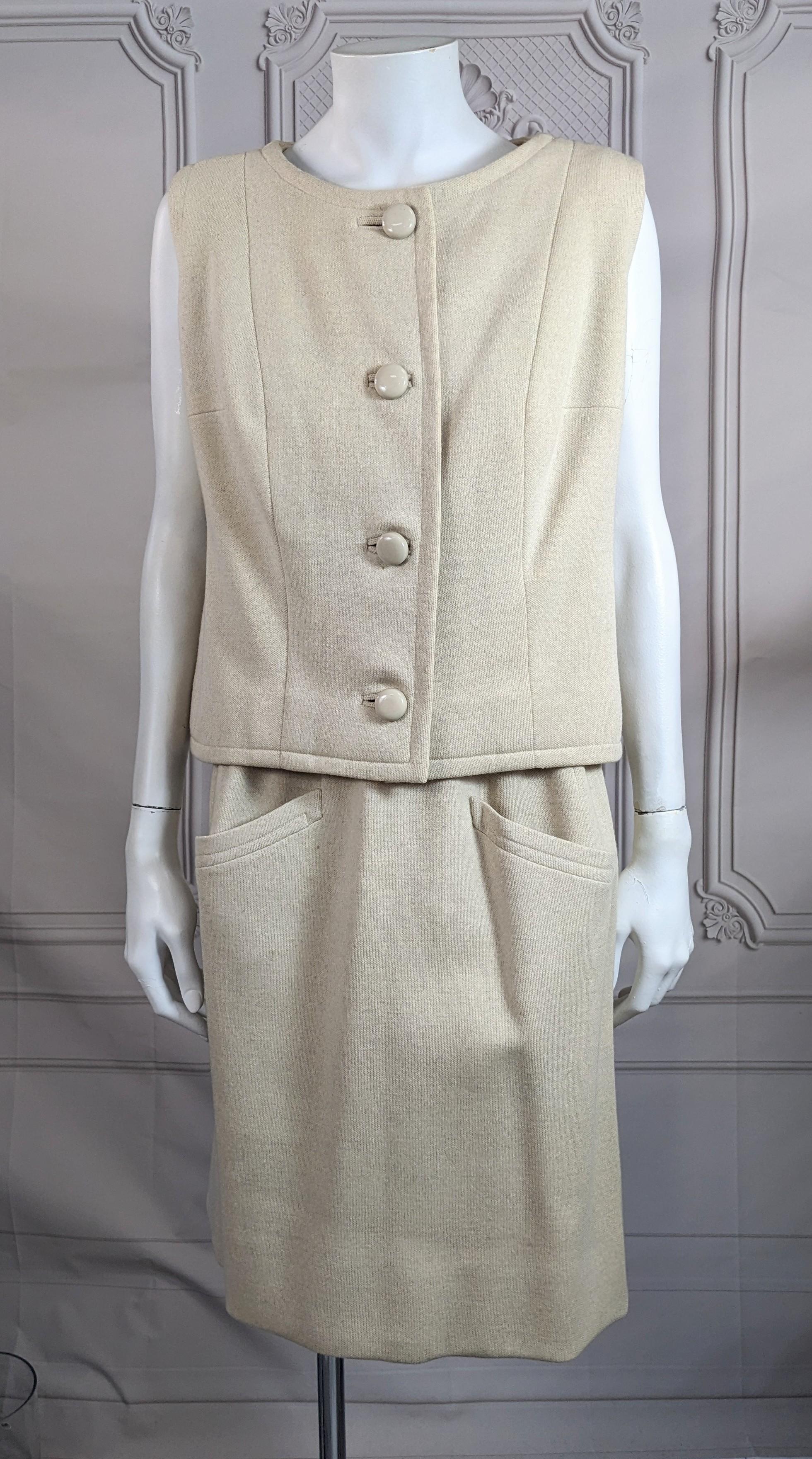 Eleganza e raffinatezza dell'ensemble Eisa in jersey di lana color avena di Balenciaga degli anni '60. Top senza maniche dalla linea a principessa con bottoni tono su tono e asole a filo. La parte superiore termina esattamente in corrispondenza del 