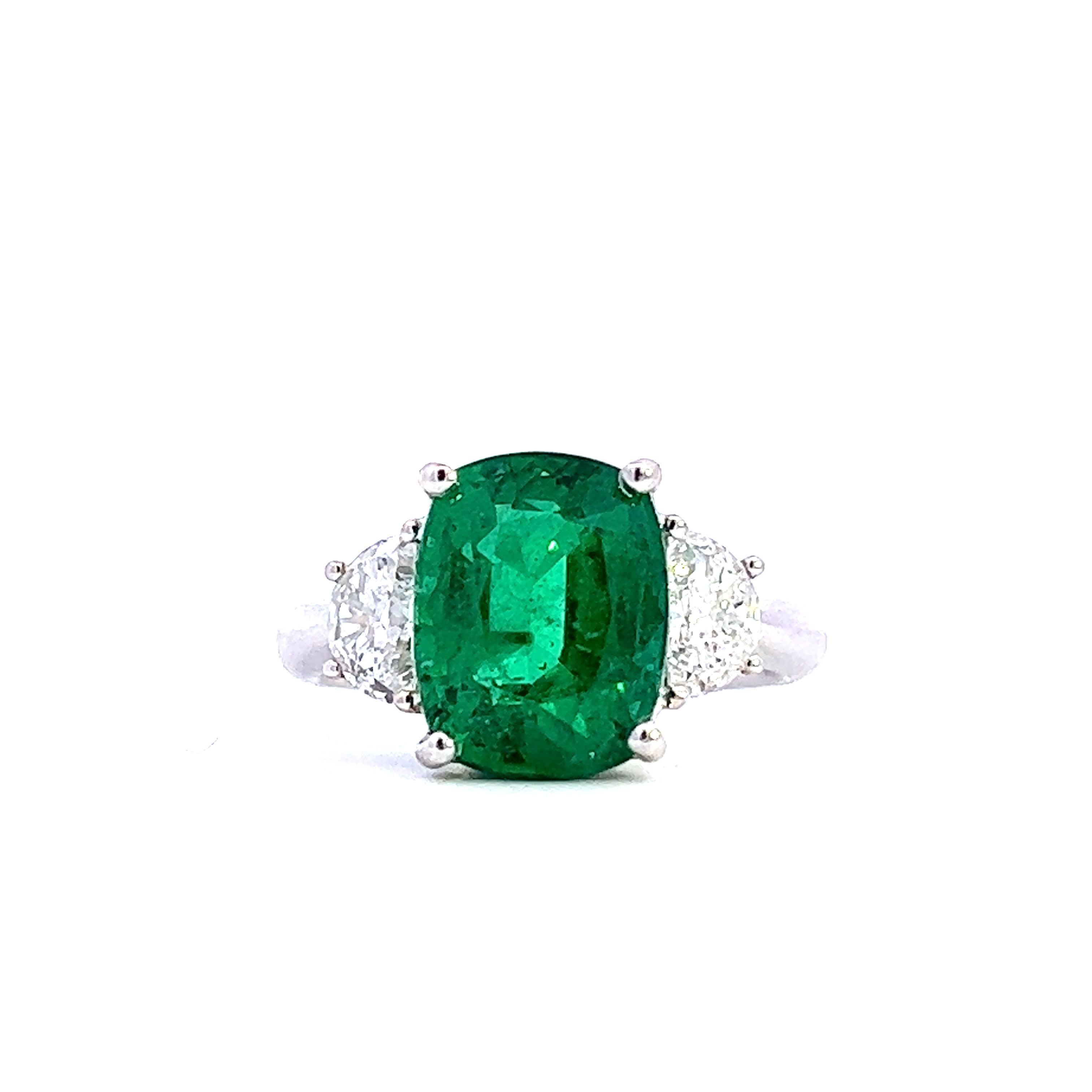 Entdecken Sie die Faszination dieses atemberaubenden Smaragdrings mit einem leuchtend grünen Edelstein in der Mitte, flankiert von funkelnden Diamanten. Dieses mit Präzision gefertigte Stück ist perfekt für alle, die Luxus und Eleganz zu schätzen