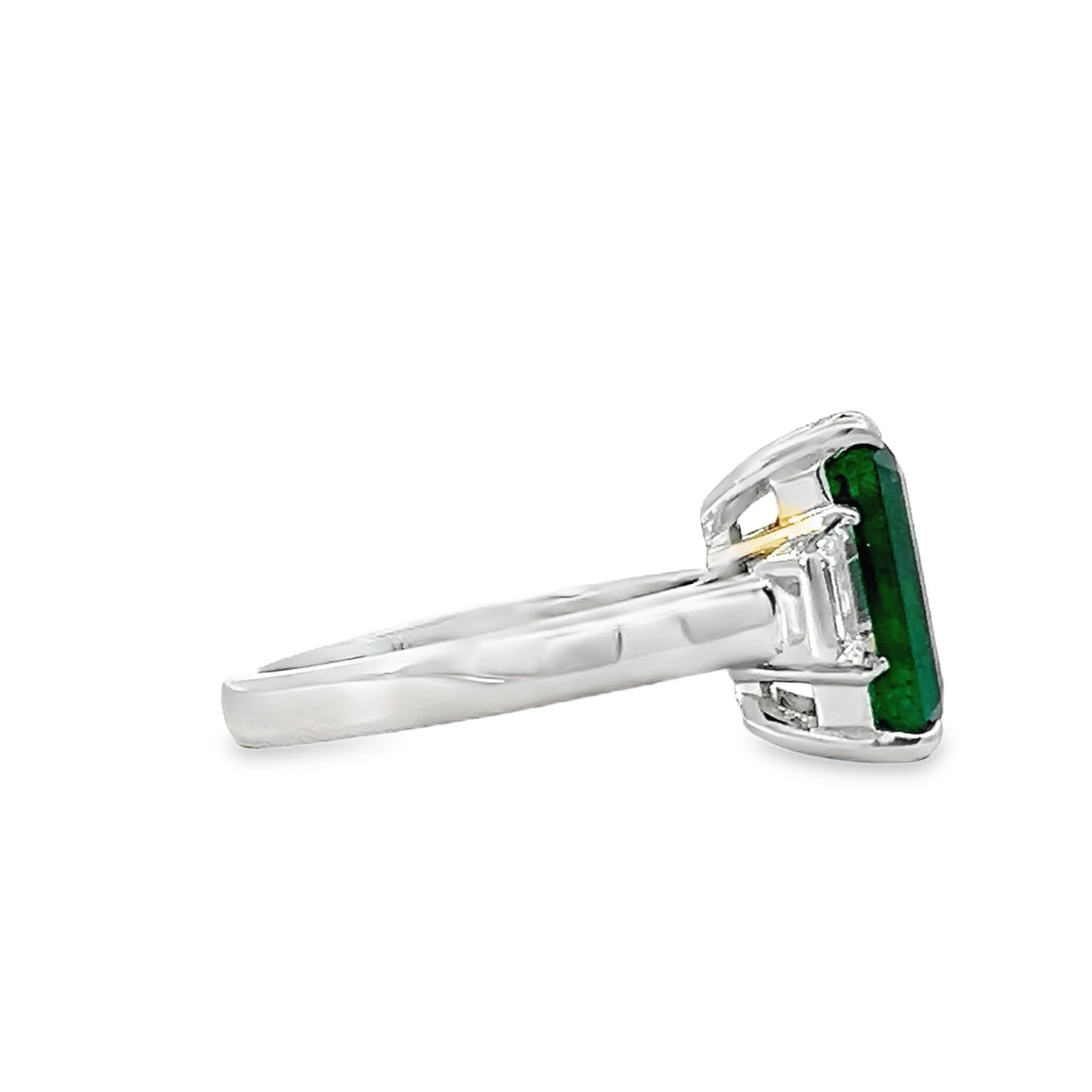 Dieser exquisite Ring zeigt einen atemberaubenden Smaragd-Edelstein, der in einem intensiven Grünton erstrahlt. Der zentrale Stein ist elegant in ein makelloses Silberband eingefasst, das von kleineren Akzentsteinen flankiert wird, die seine