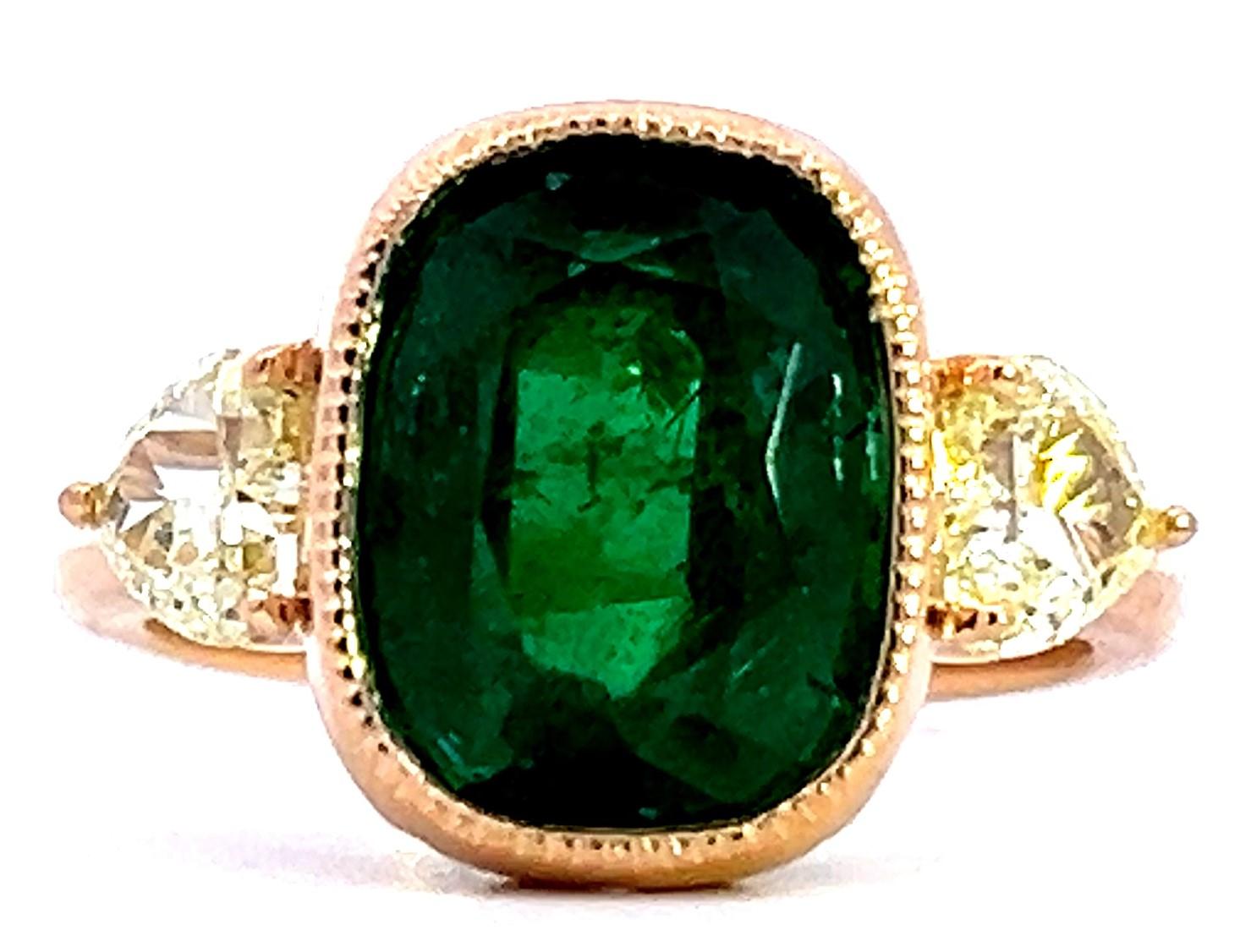 Cette bague exquise est ornée d'une superbe émeraude coussin de 11,5 x 9 mm, flanquée de deux diamants étincelants. La riche teinte verte de l'émeraude est magnifiquement complétée par les tons chauds du bracelet en or, créant ainsi une pièce