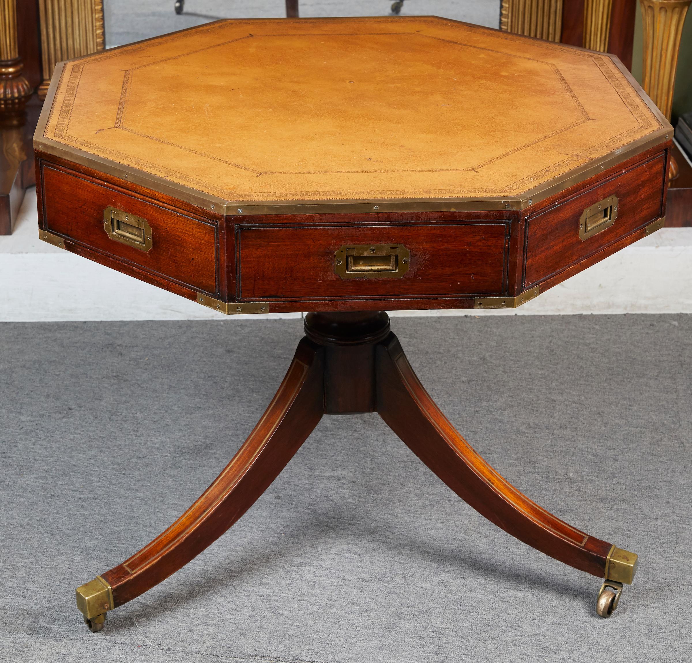 Elegant Campaign style mahogany octagonal drum table fitted with typical flush mount brass fittings and tooled leather top, resting on a single pedestal fitted with three saber legs ending with square brass casters .
Size of top from flat side to