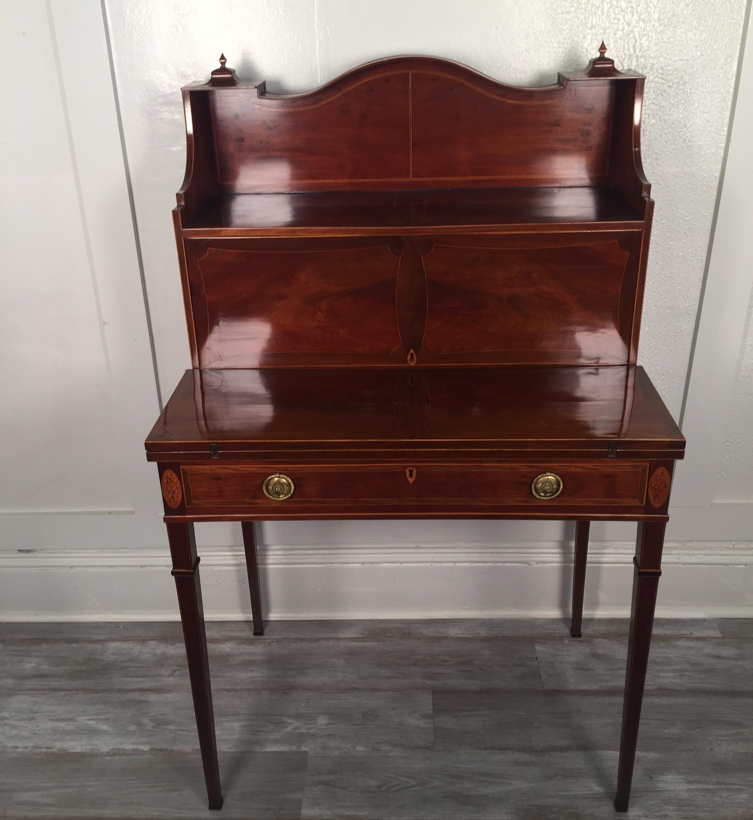 A small scale mahogany and satinwood inlaid desk. The top with display surface with a concealed section of small drawers. The work surface that flips open with the original leather covering. There is on long drawer at the apron. The desk, resting of