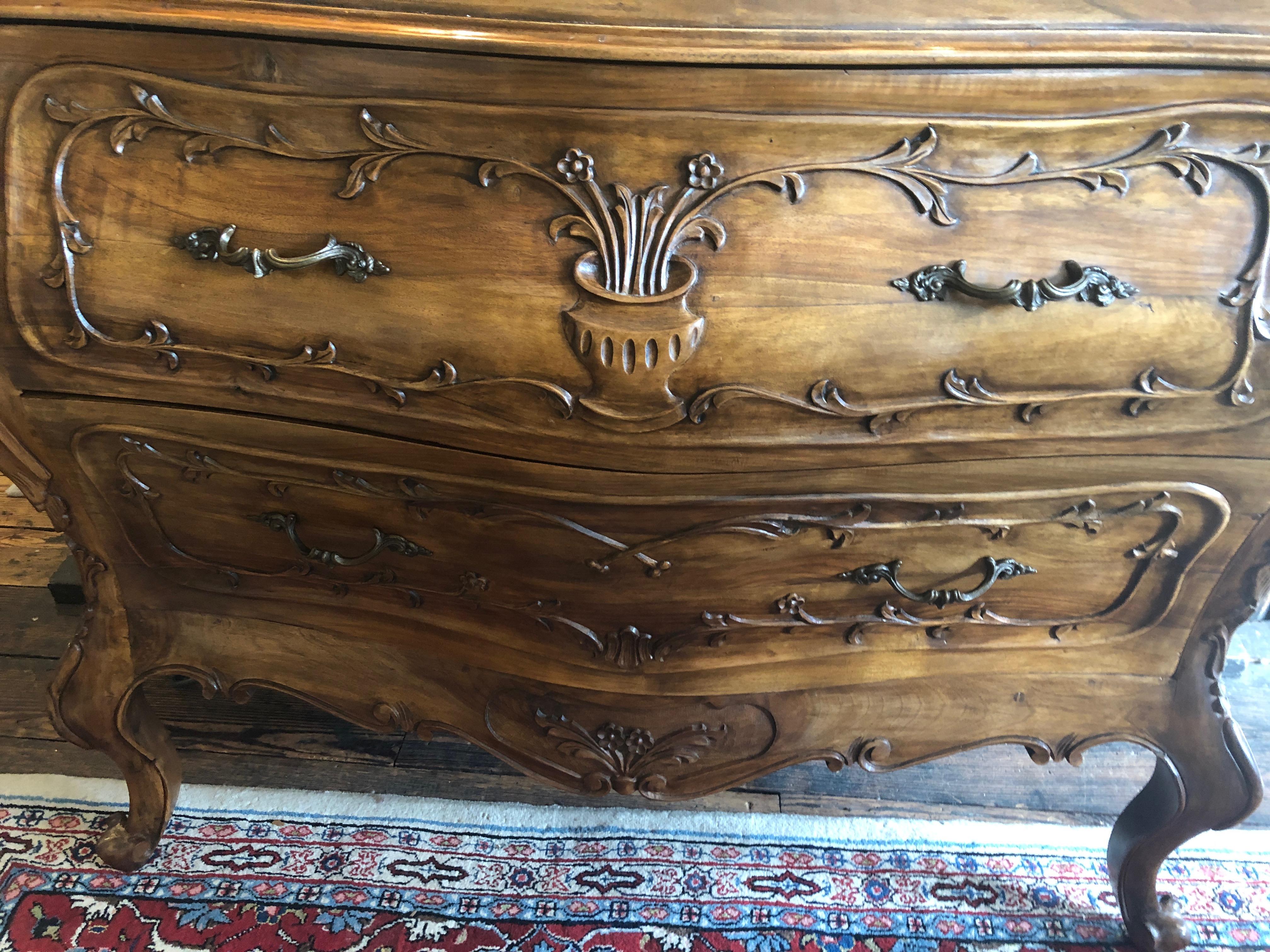 Absolutely beautiful carved wood bombay style two-drawer commode having gorgeous grain, decorations including vase of flowers and acanthus leaves on the cabriole legs, and lovely original brass hardware.