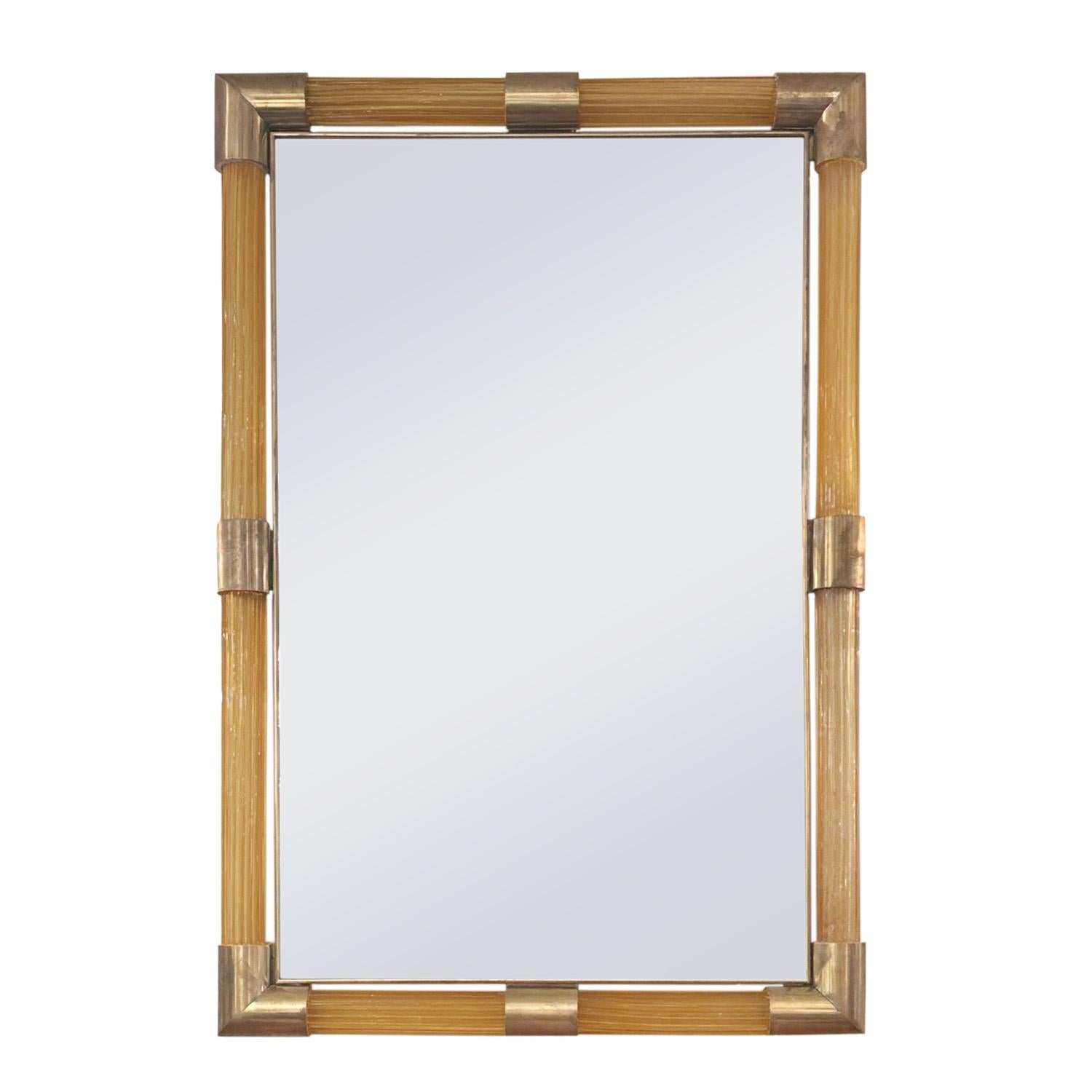 Hand-blown Amber color Murano fluted glass rod framed mirror with un-lacquered brass cuffs at corners and midpoints.
This mirror features a unique fluted design crafted from Murano glass rods, adding a touch of elegance and sophistication to your