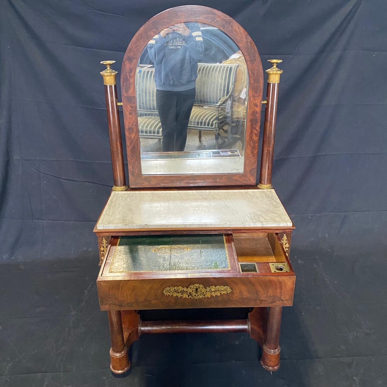 Beautiful French 19th century Empire marble top mahogany dressing table or vanity featuring an arch design adjustable mirror held by two wood columns accentuated by brass finials on top, intricate bronze details throughout the entire piece, and a