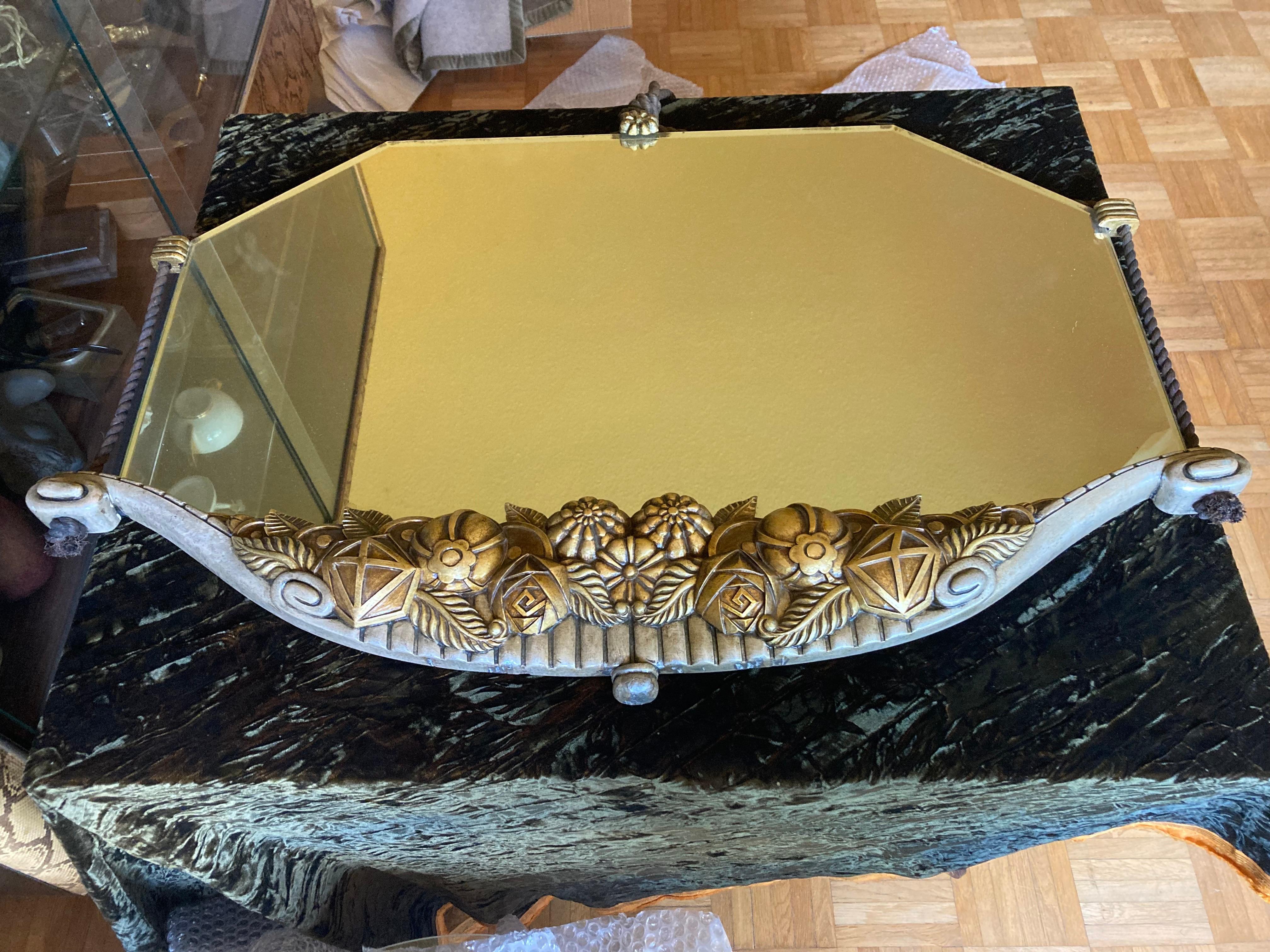 Elegant French Art Déco Wall Mirror by Maurice Roger & Ed. Feron. 1920s.
Hand carved floral wood mount is gilded and silver plated. Mirror with faced cut. 
Original cord suspension without tassels.
The mirror is documented and illustrated in a