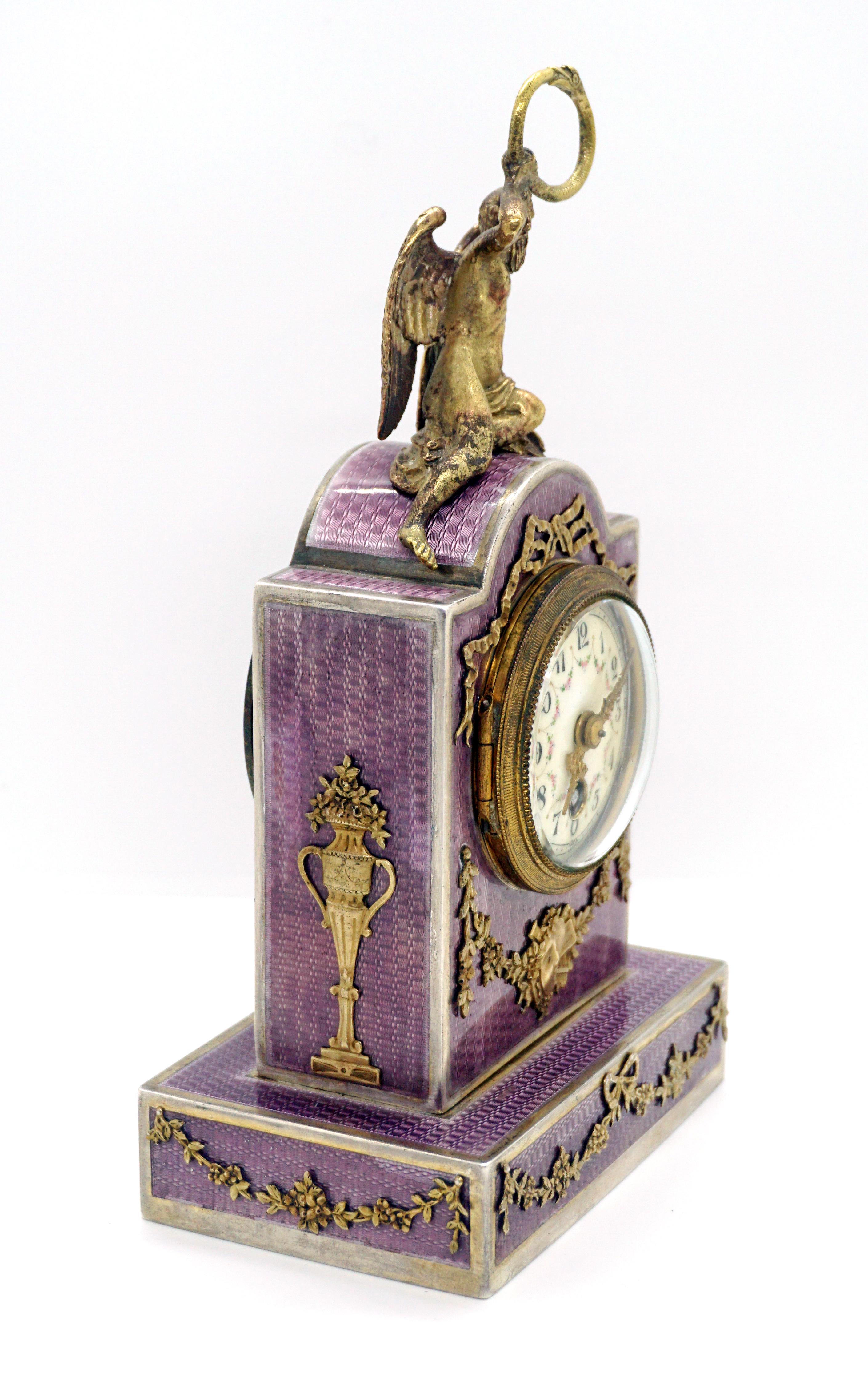 Exquisite French silver enamel table clock from the period circa 1900

Silver case with violet gouilloche enamel, porcelain dial with painted Arabic numerals, enameled floral decor and gold hands. Richly decorated with floral applications made of