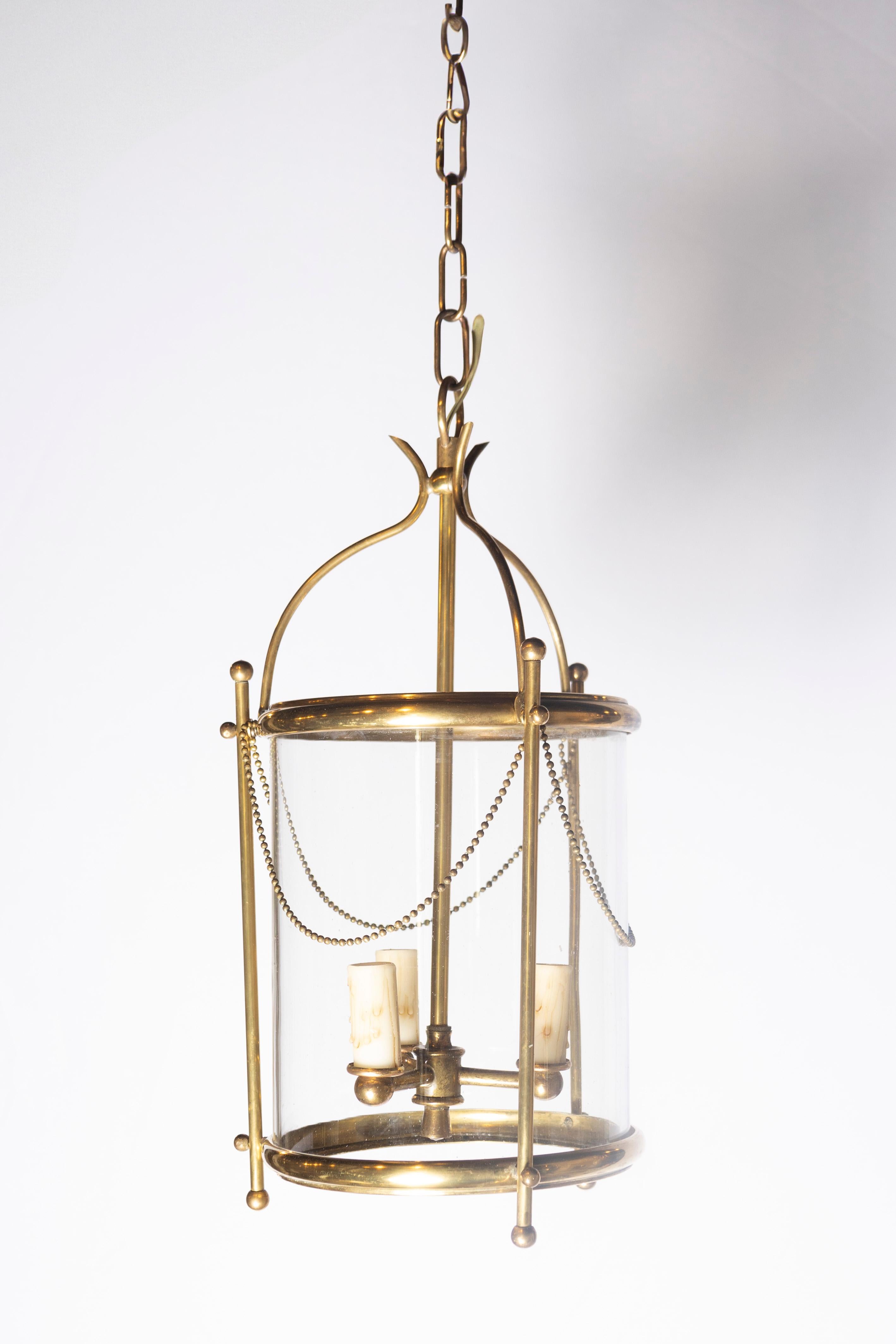 Lustre lanterne en laiton français des années 1940, raffiné et intemporel, doté d'un design saisissant mais discret qui allie l'élégance classique à la simplicité moderne. Le cadre de la lanterne est composé de supports en laiton gracieusement