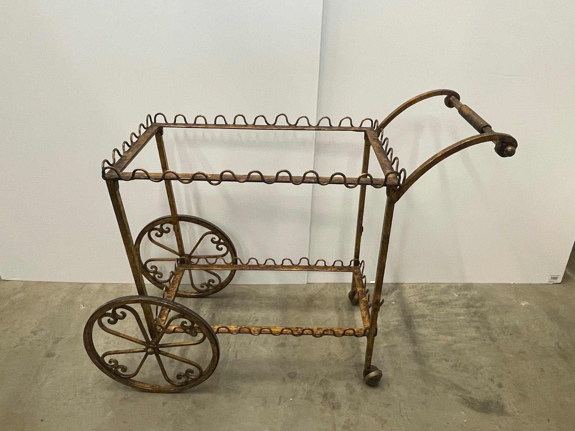 An unusual form and particularly elegant French gilt iron mid century modern bar cart having two tiers with decorative wave like galleries around the periphery. Top shelf is clear glass; bottom shelf is aged mirror. Wheels are superbly decorative