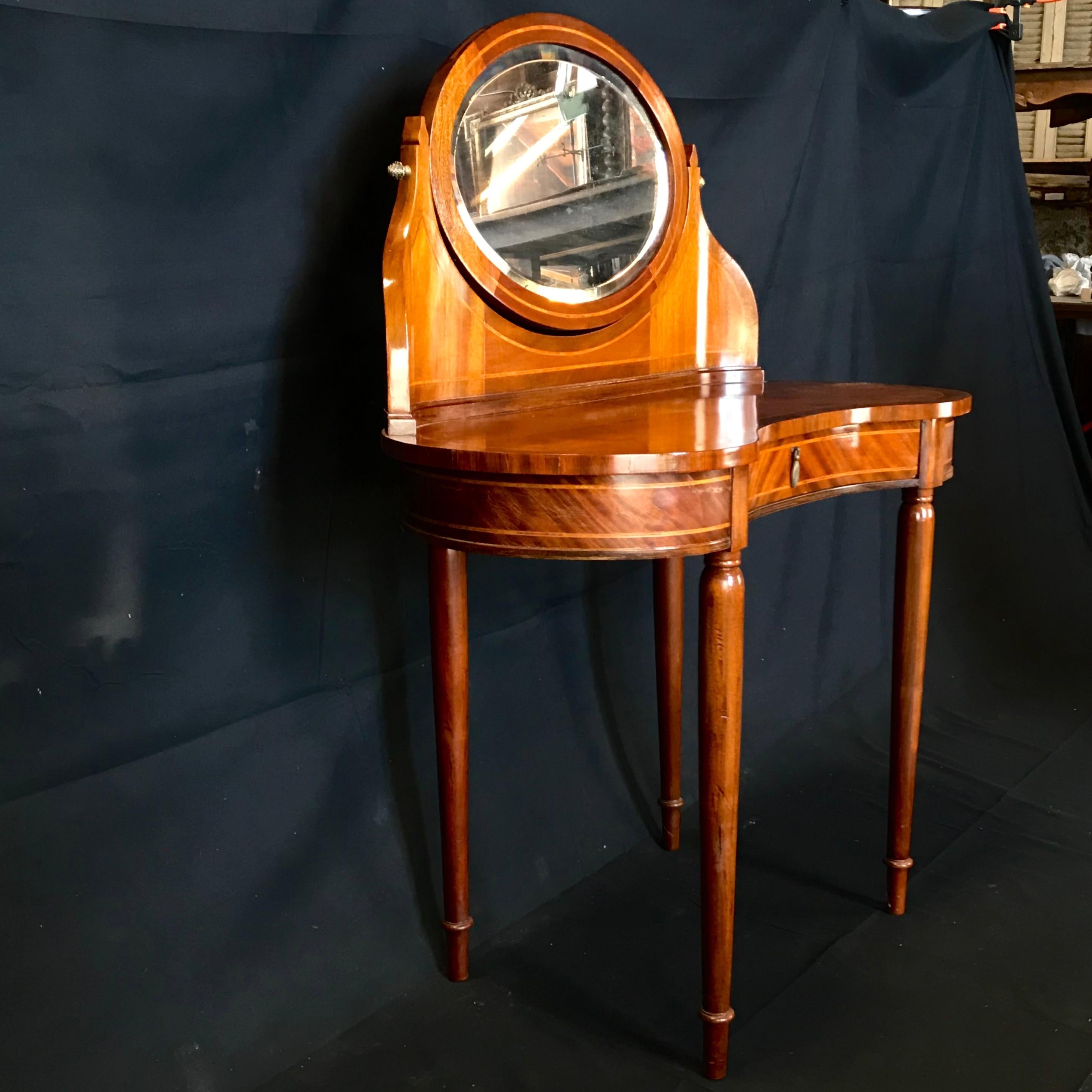 A French walnut inlaid dressing table, circa 1930. This fine dressing table has a kidney shaped top with gilt-bronze mirror support and a superstructure supporting an oval beveled mirror, above one center frieze drawer and raised on delicate