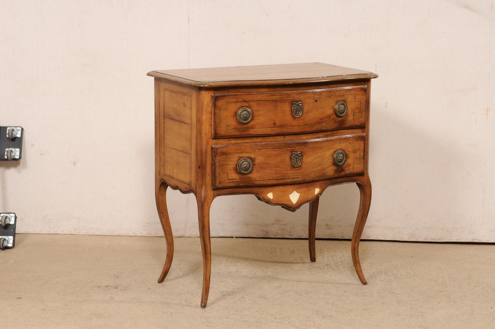 A French Louis XV raised two-drawer commode, with its original hardware, from the early 19th century. This antique wooden chest from France features a subtly curved serpentine top and front facade, and case which houses two drawers, a nicely carved