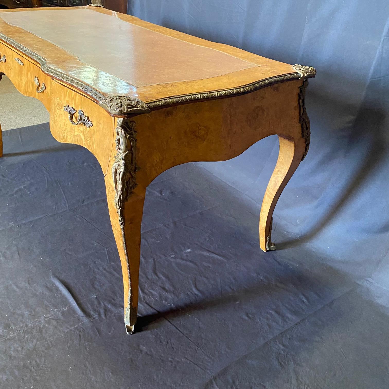 An outstanding Louis XV-style burlwood bureau plat, having a shaped leather-inset top above an elaborate frieze with three disguised drawers, all on cabriole legs, the whole embellished with opulent ormolu mounts. Shaped and finished on the back