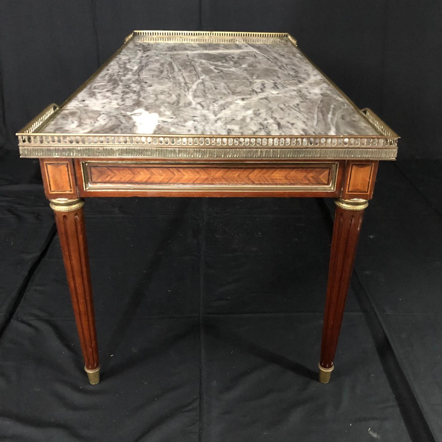 Classic Louis XVI style walnut coffee table with beautiful marble top and gold brass fretwork gallery. Great size and rich grey and white marble top. Marble has a professionally repaired crack (see photos) that is well camouflaged with the graining.