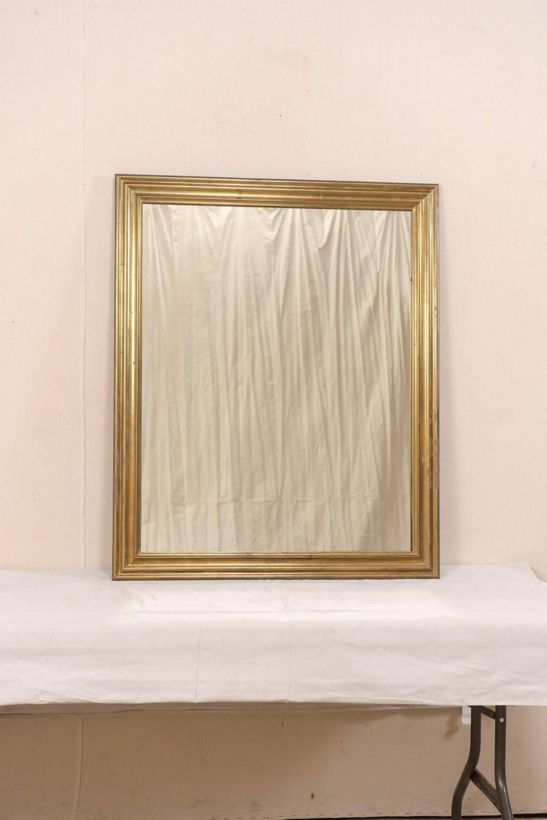 A French mirror with brass surround from the mid-20th century. This simple and elegant vintage French mirror features a rectangular shape with brass surround, which has a lovely patina throughout. This is a good sized mirror, standing at over 3.5 ft