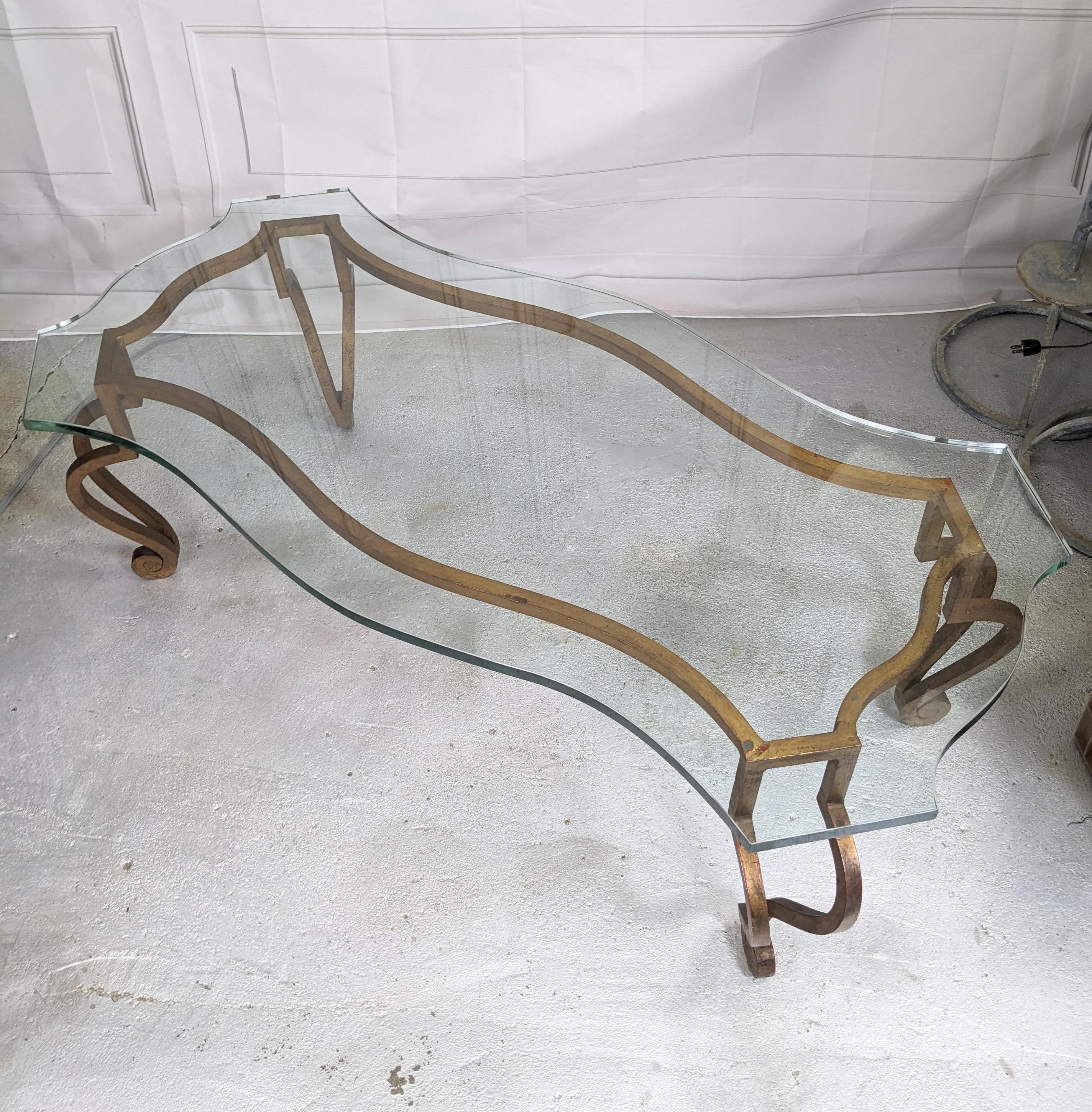 Elegant French Mid Century Gilt Iron Coffee Table in the Jansen style of gilt forged iron with fancy cut thick glass scalloped top. Typical dramatic lines in the Mid Century French style which is timelessly elegant. Nicely patinaed hand gold leaf