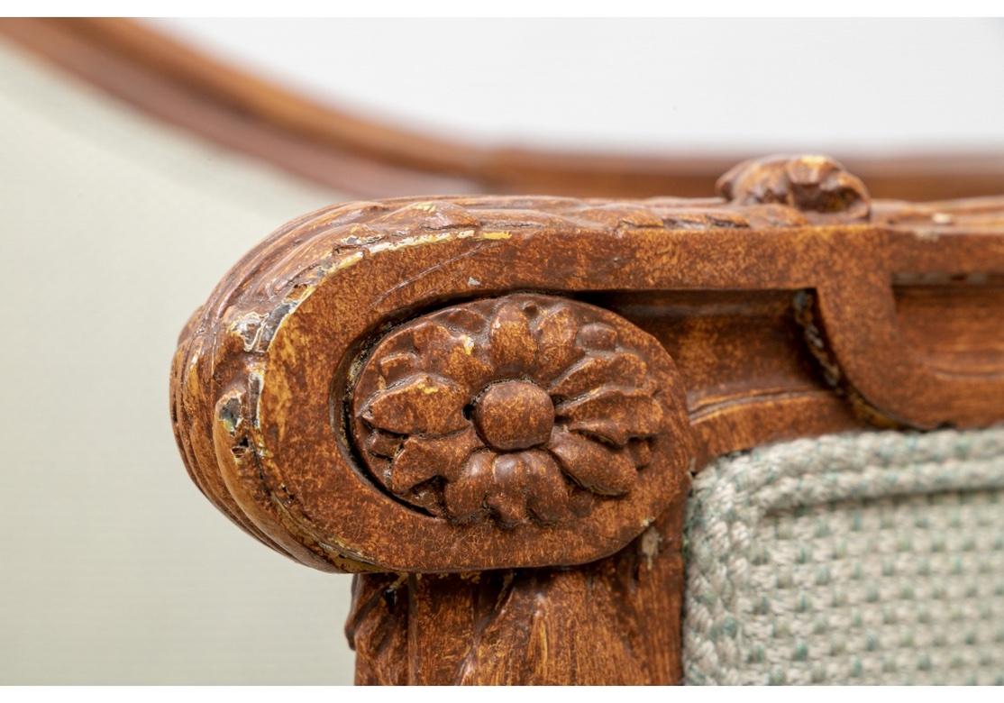 A large and deep French Style sofa with elaborately carved and shaped frame with a floral basket crest. The arm ends with carved acanthus leaves and bell flowers along the front frame and skirt. Raised on short fluted tapering legs in front and