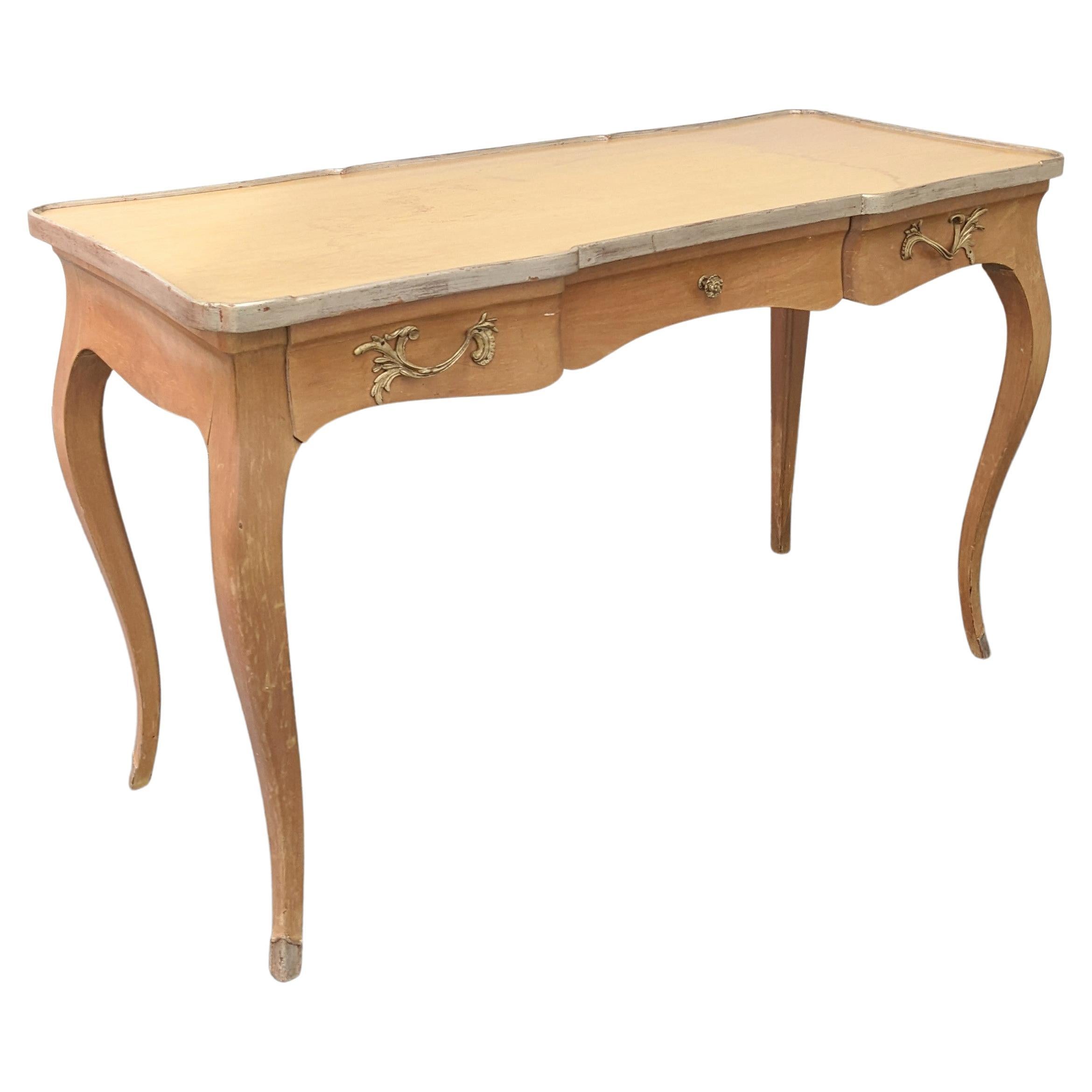 Elégant bureau de style français aux lignes Louis XV en bois blond avec bord de table et pieds peints à la feuille d'argent. 3 tiroirs. Le plateau en verre est inclus (sans image).
Mesures : 20