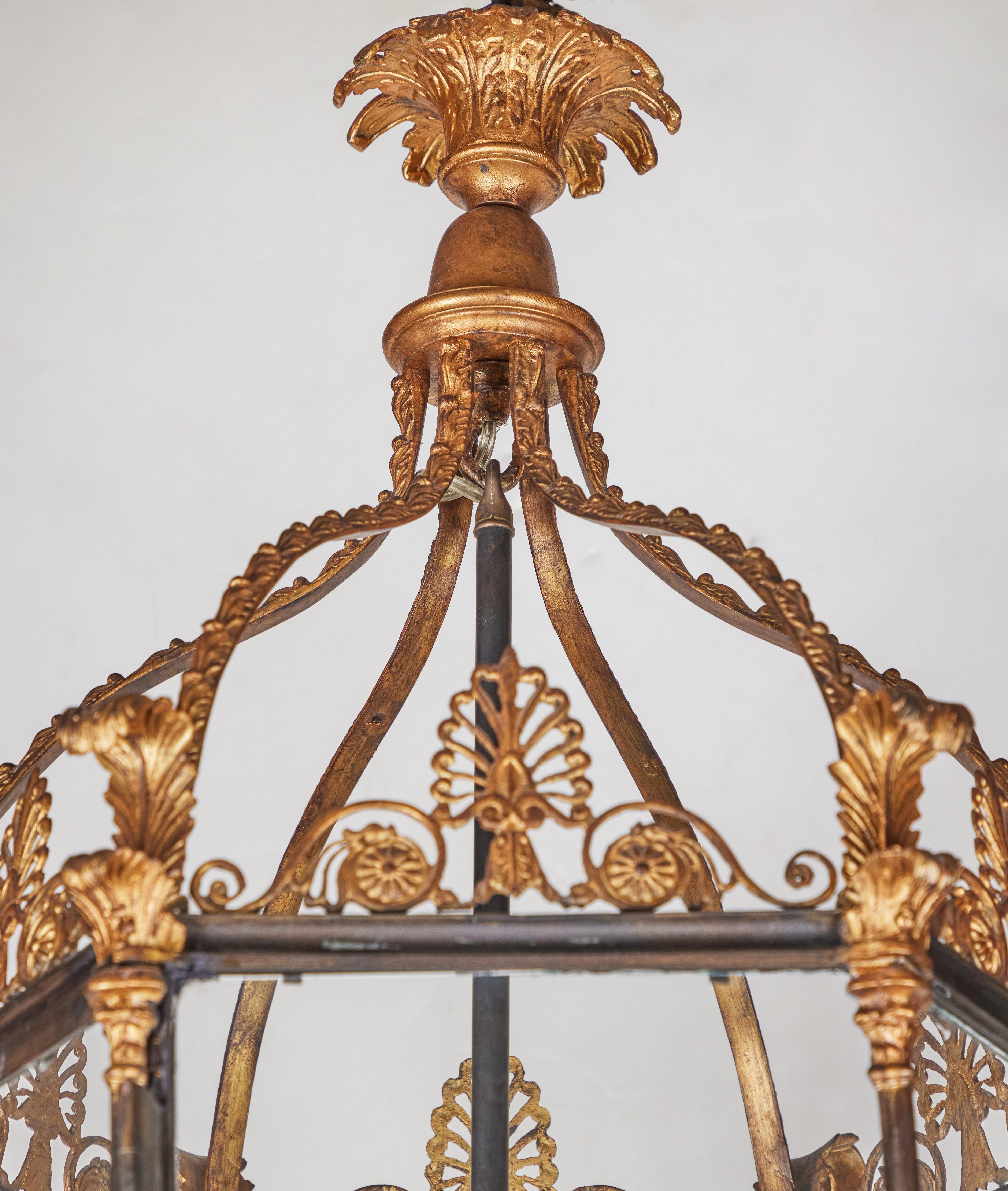 Hexagonal, cast iron and gilt bronze, glass encased, four-light lantern. The slender pillars comprising the body, rises to curling, gilt bronze leaves beneath a canopy featuring scrolling foliate forms all surmounted by a ceiling medallion of the