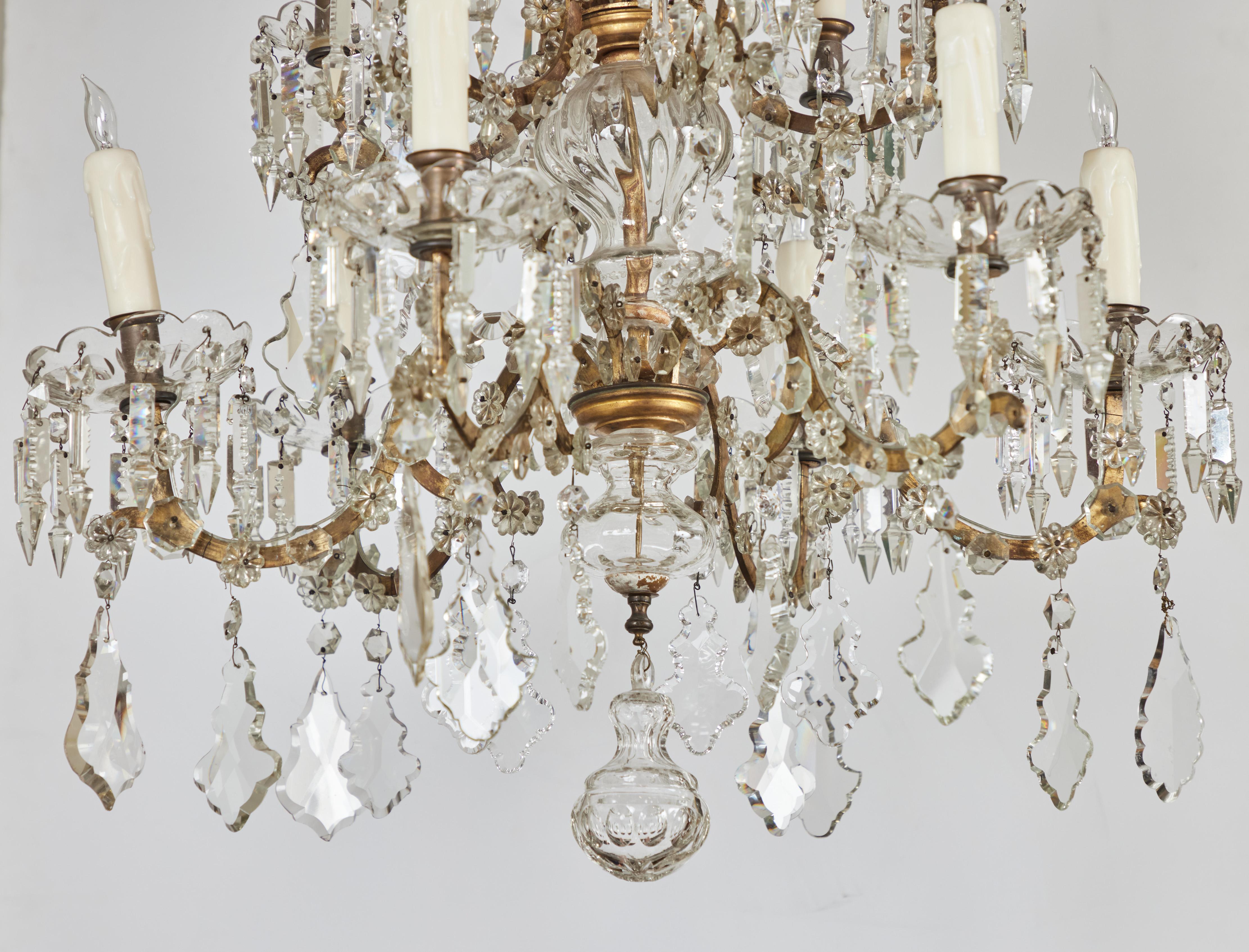 Elegant lustre en métal doré et cristal à 12 lumières. 2 Designs de placards à volutes et de bobeches dramatiques avec des pendentifs suspendus. Câblé pour les États-Unis.
