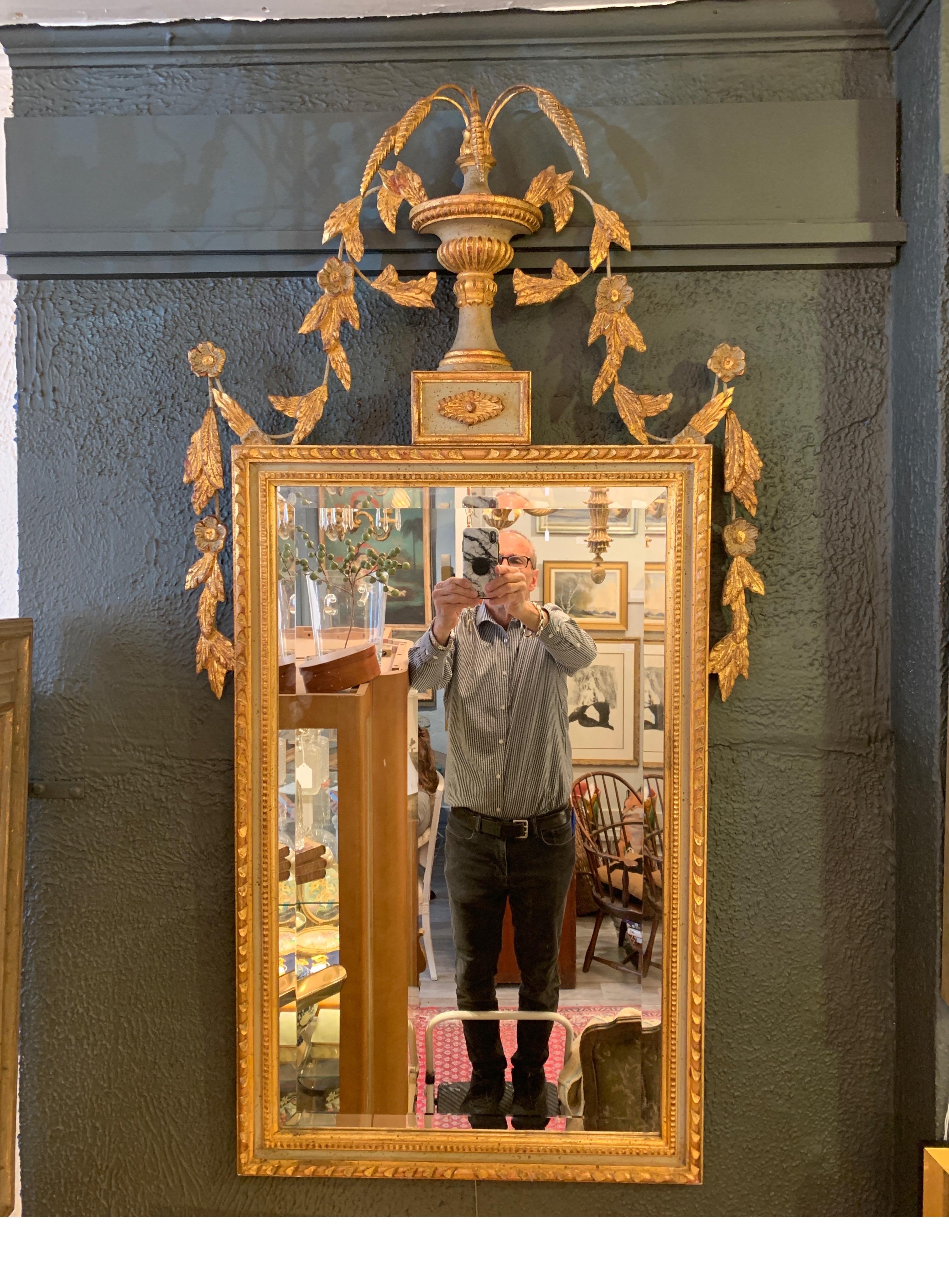 A beautiful giltwood mirror with beveled glass. The elaborate top with urn and wheat plumes with cascading floral down the top and sides with a light sage green accent on the frame, Italy, mid-20th century.