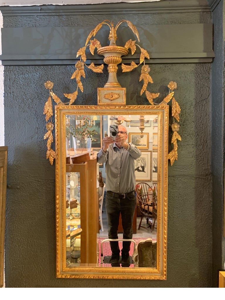 A beautiful giltwood mirror with beveled glass. The elaborate top with urn and wheat plumes with cascading floral down the top and sides with a light sage green accent on the frame, Italy, mid-20th century.