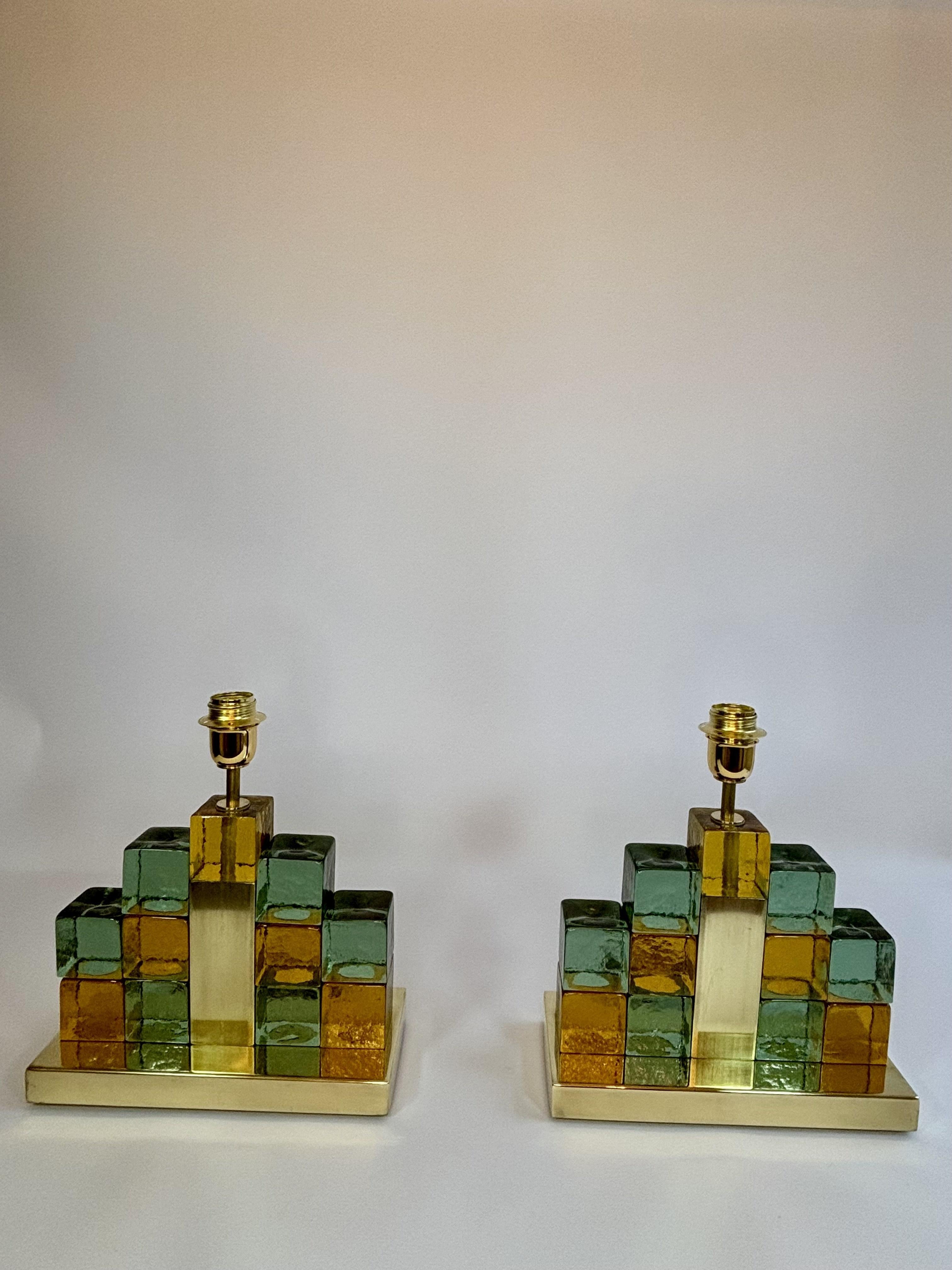 Prova il fascino dell'artigianato italiano con questa coppia unica di lampade da tavolo contemporanee. Ogni pezzo è realizzato meticolosamente con una solida base in ottone, sormontata da cubi in vetro di Murano. Le lampade sono state realizzate nel