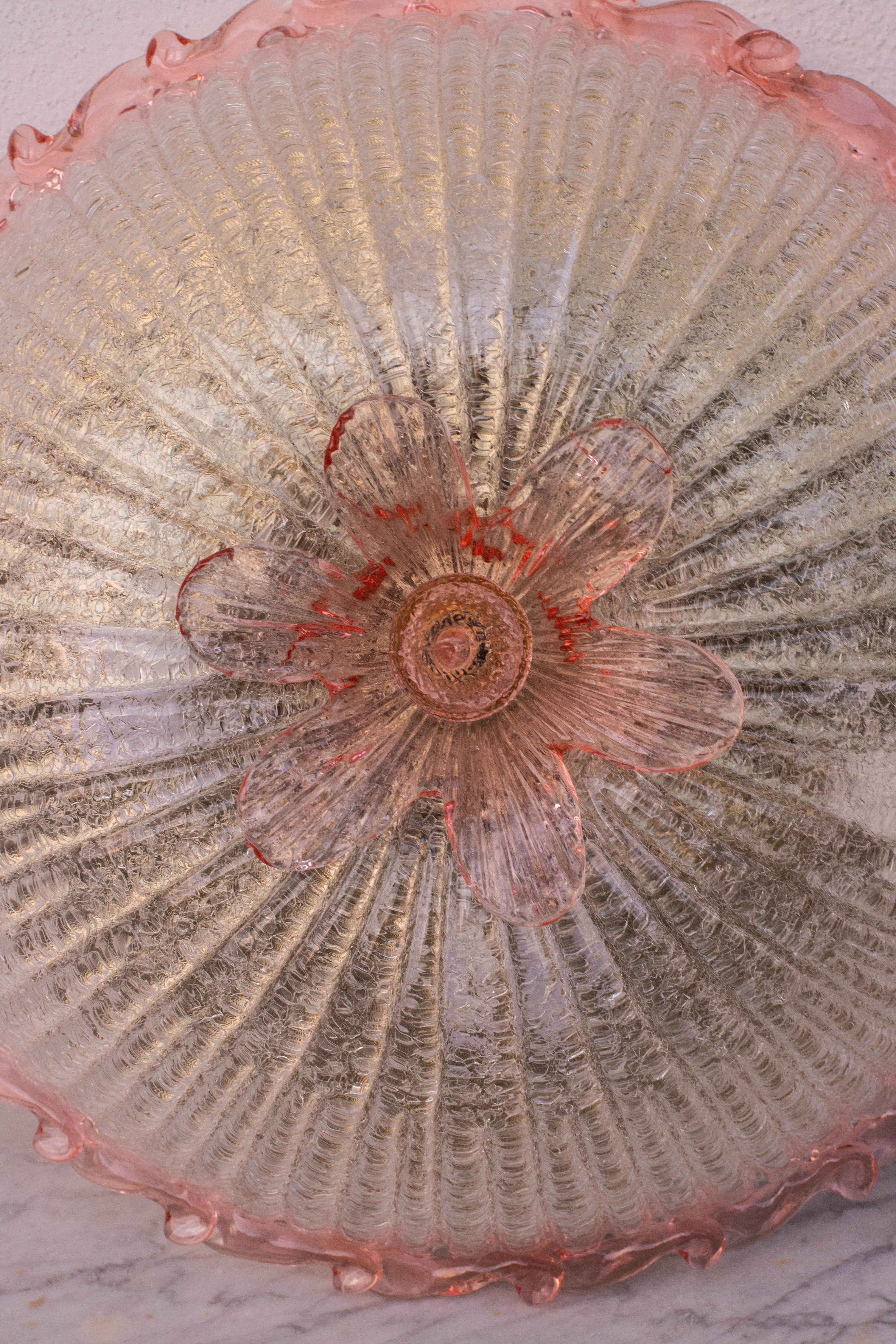 Magnifique plafonnier de Murano rose et transparent/doré.
Le plafonnier se compose de 3 éléments en verre, de la plaque centrale et d'une belle fleur rose.
La plaque centrale est entourée d'une bande rose ondulée typique de la facture vénitienne de