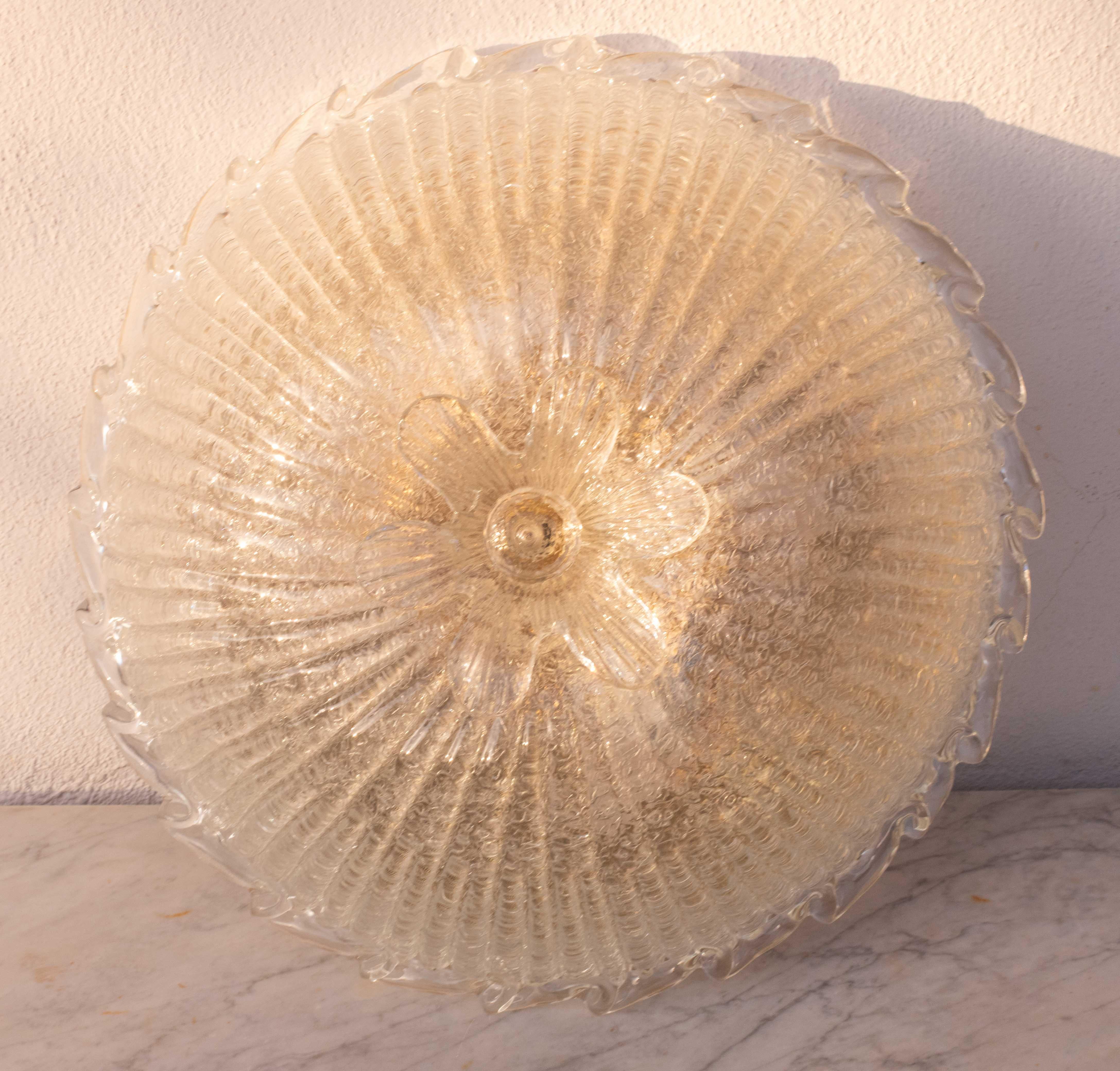 Gorgeous transparent/gold Murano ceiling light.
The ceiling light consists of 3 glass elements, the central plate and a beautiful transparent flower.
The central plate is surrounded by a wavy transparent stripe typical of Venetian Murano