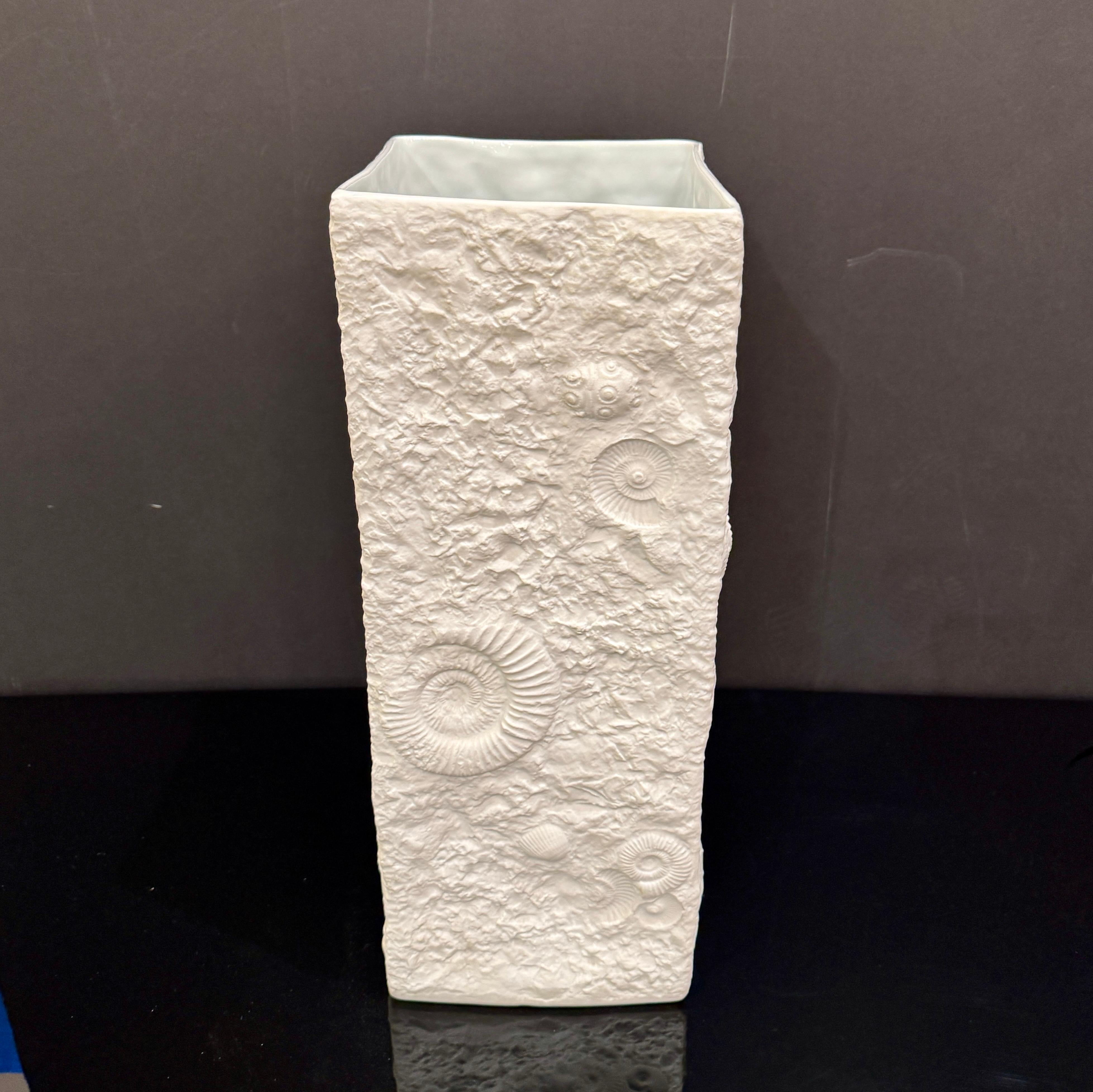 Questo splendido vaso in porcellana Bisque di Kaiser cattura la bellezza del mare con delicati motivi fossili di ammonite, elegantemente resi in una morbida finitura bianca opaca. Firmato sotto, riflette l'alta maestria del rinomato produttore di