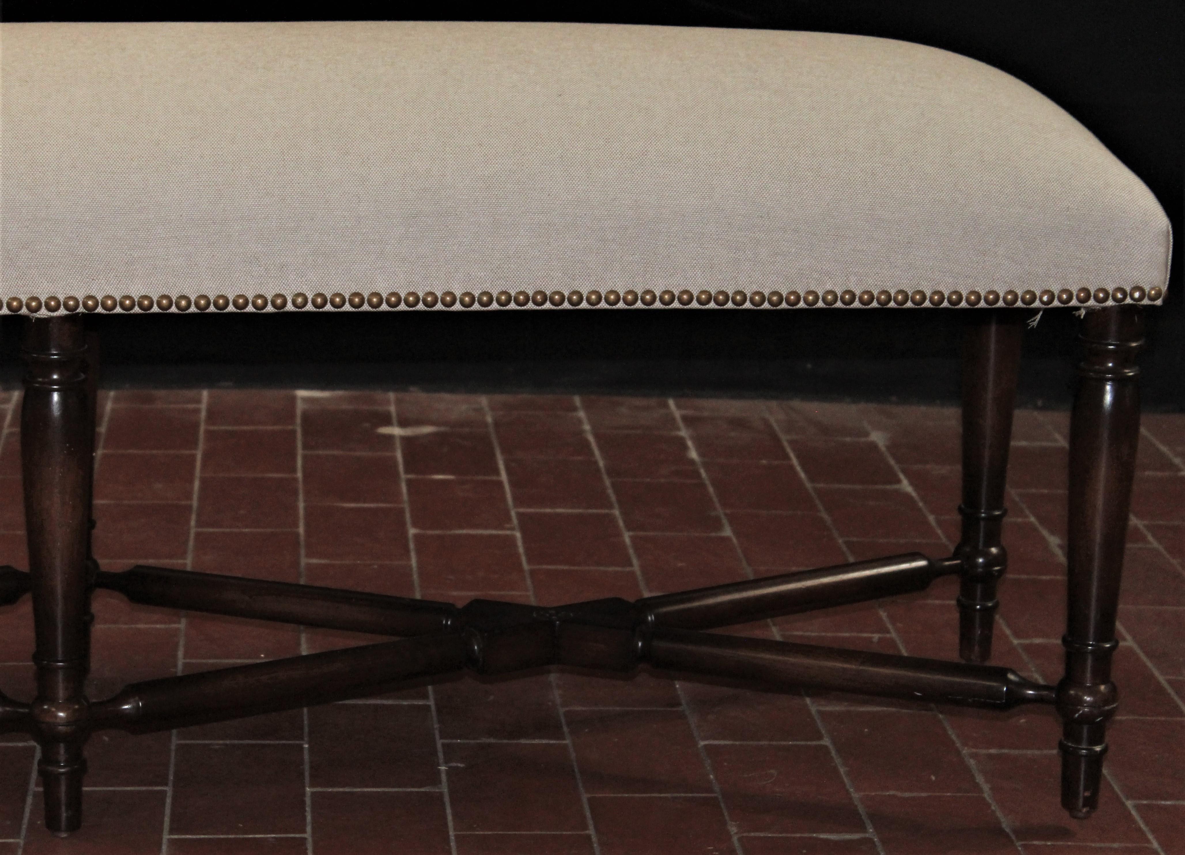 18th century style upholstered bench from England with upholstered seat in linen finished with single welt decoration, supported upon mahogany hand-turned feet.
 