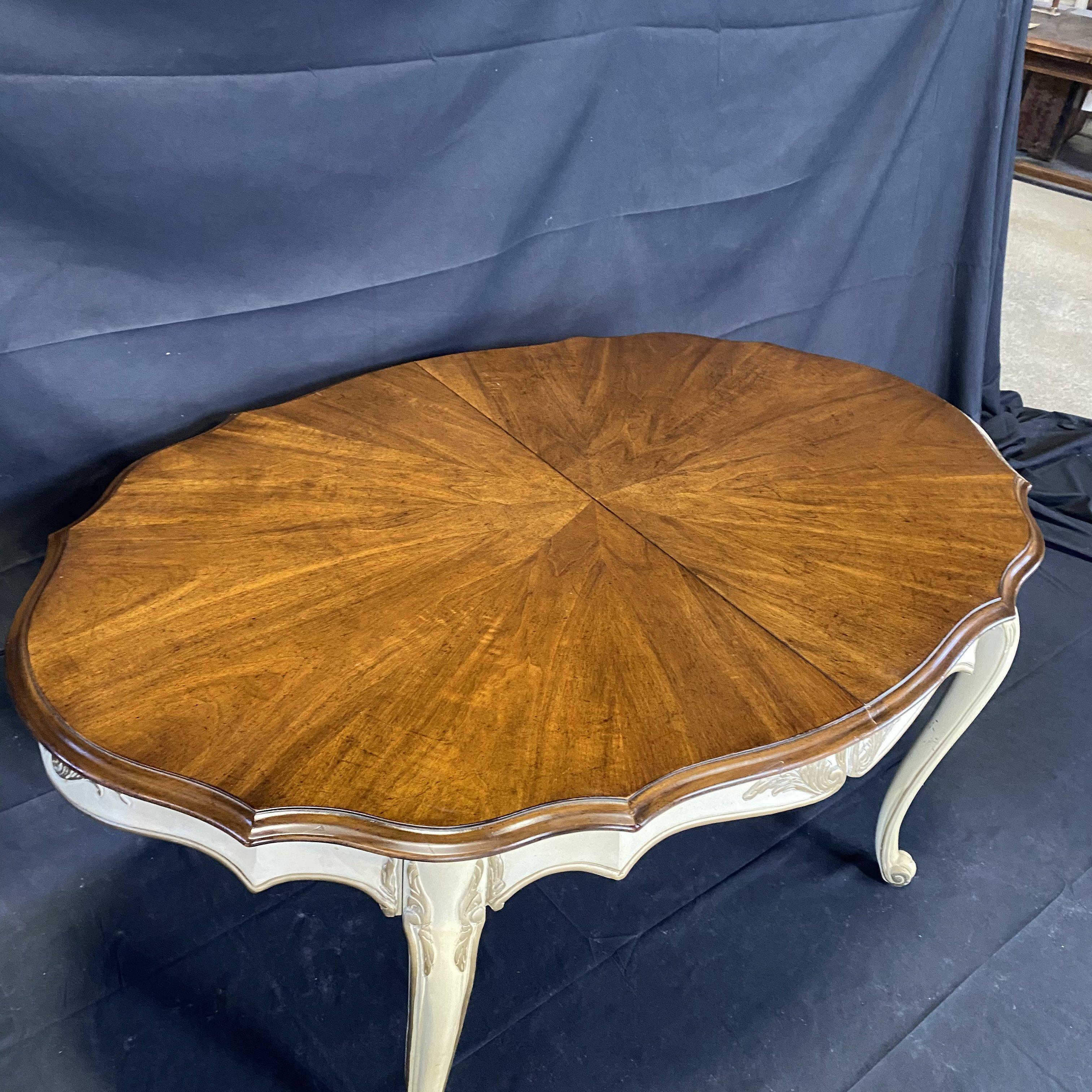 Beautiful mid century oval dining table with two leaves and an ivory painted scalloped apron with carved acanthus leaves and cabriole legs with spines ending at the top with splayed leaves. The apron and legs have banded borders. The table extends