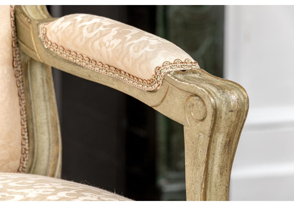 Ein klassisches Fauteuil im Stil Louis XV mit einem geschnitzten und bemalten Rahmen in einem grau-grünen Ton mit antik vergoldeten Details. Mit  floralem Wappen und geschnitzten Rippenarmen. Die geformte Sitzschiene ist mit geschnitztem Blattwerk