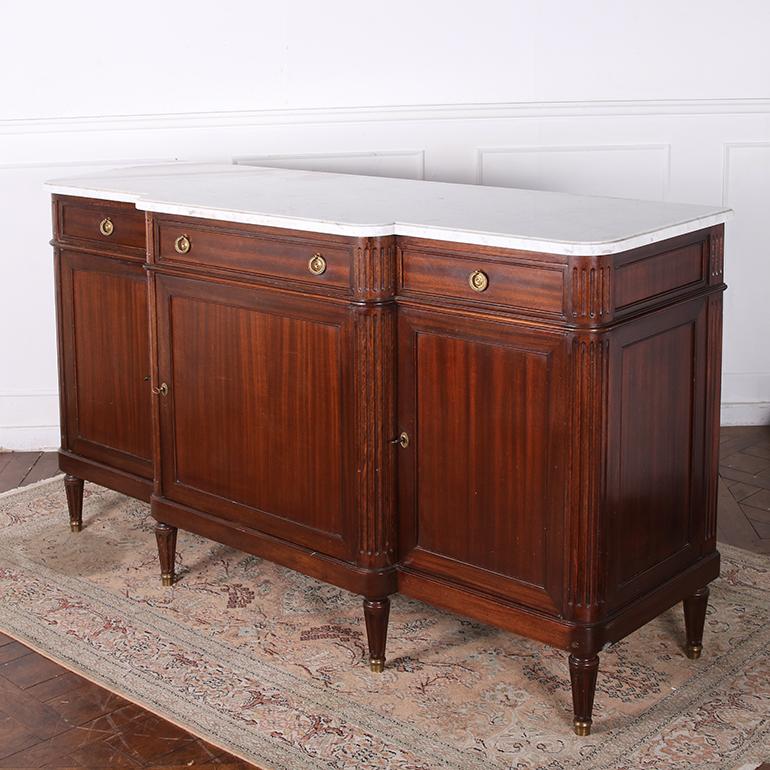 An elegant, French, Louis XVI style mahogany, three door & three drawer buffet with original shaped marble top.  At the center is a single large cabinet door with a simple recessed panel and brass keyhole escutcheons, flanked by cabinet doors