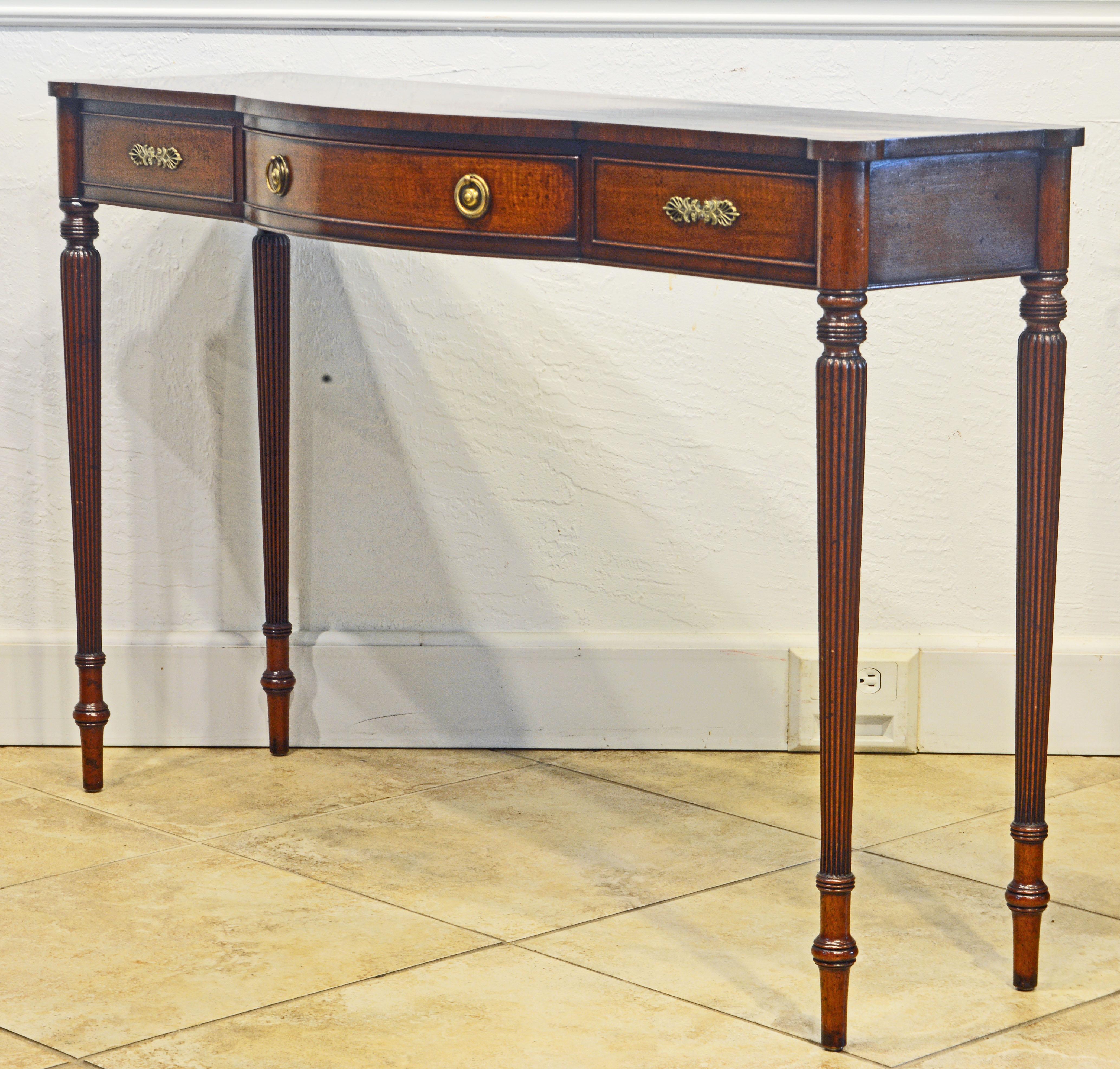 Of slender and elegant proportions this bench made console table features a satinwood inlaid mahogany top with 'ears' in each corner corresponding with four typical turned and fluted baluster shape legs. The frieze holds a central bow front drawer