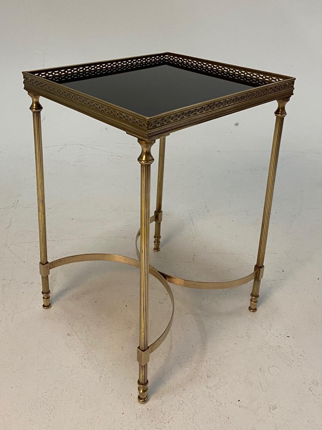 Classically elegant French Maison Jansen Hollywood Regency style cocktail end table having pierced brass gallery, tapered legs and contrasting black glass table top.