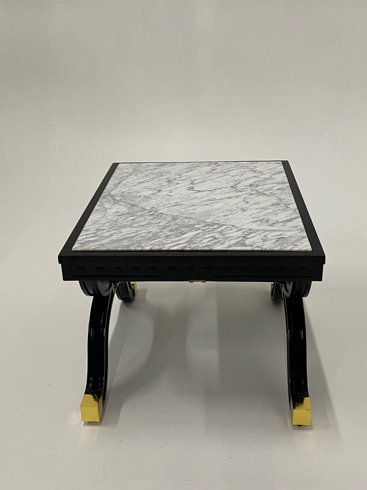 Hollywood Regency glamorous ebonized and giltwood end table having fancy brass feet and pristine marble top.
