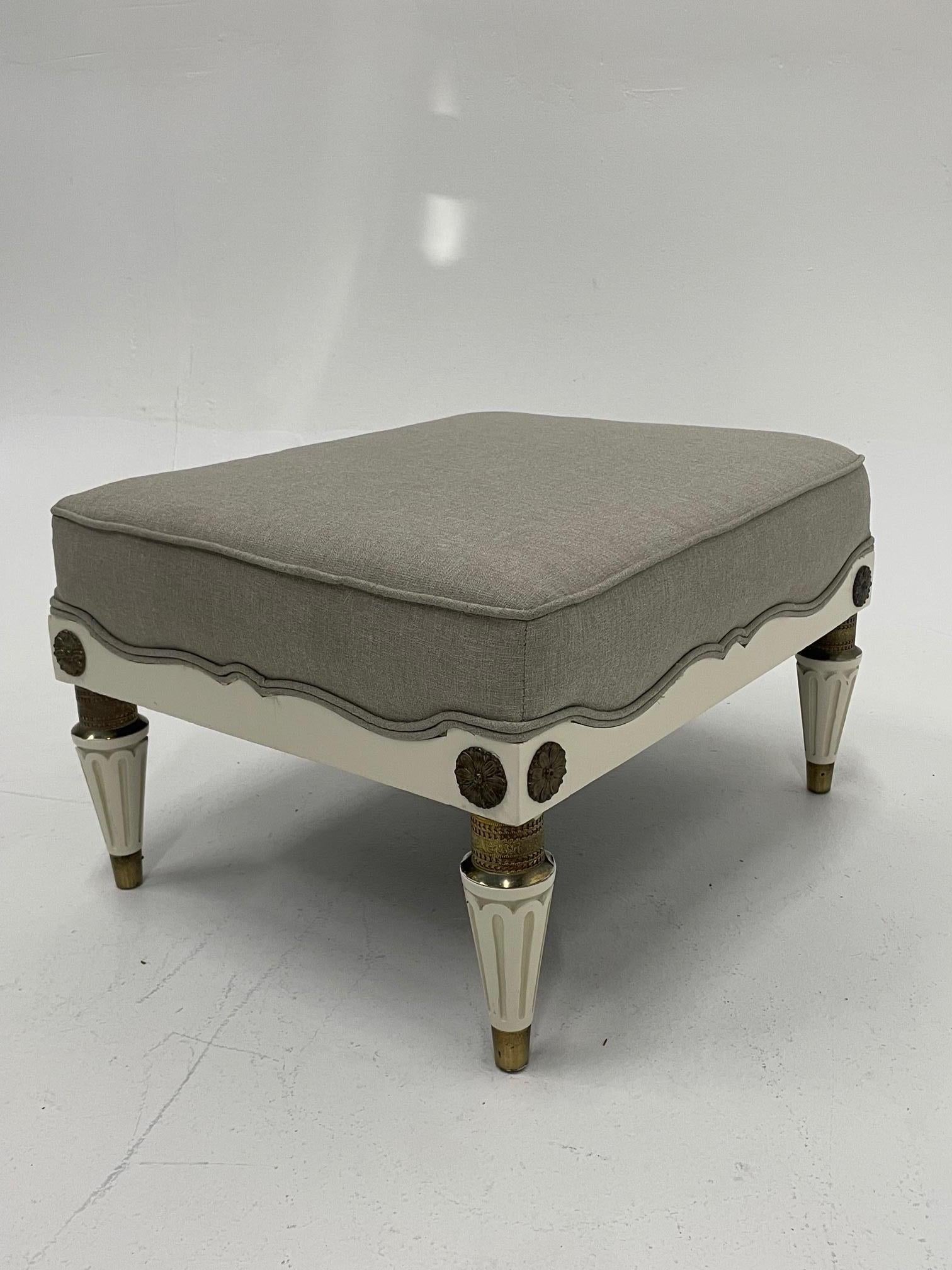 A very classy and unusually stylish French ottoman having unusual blend of white laquered wood embellished by brass mounts, decoration on the tapered fluted legs and capped feet. Newly upholstered in high end linen and pretty scalloped lines at the