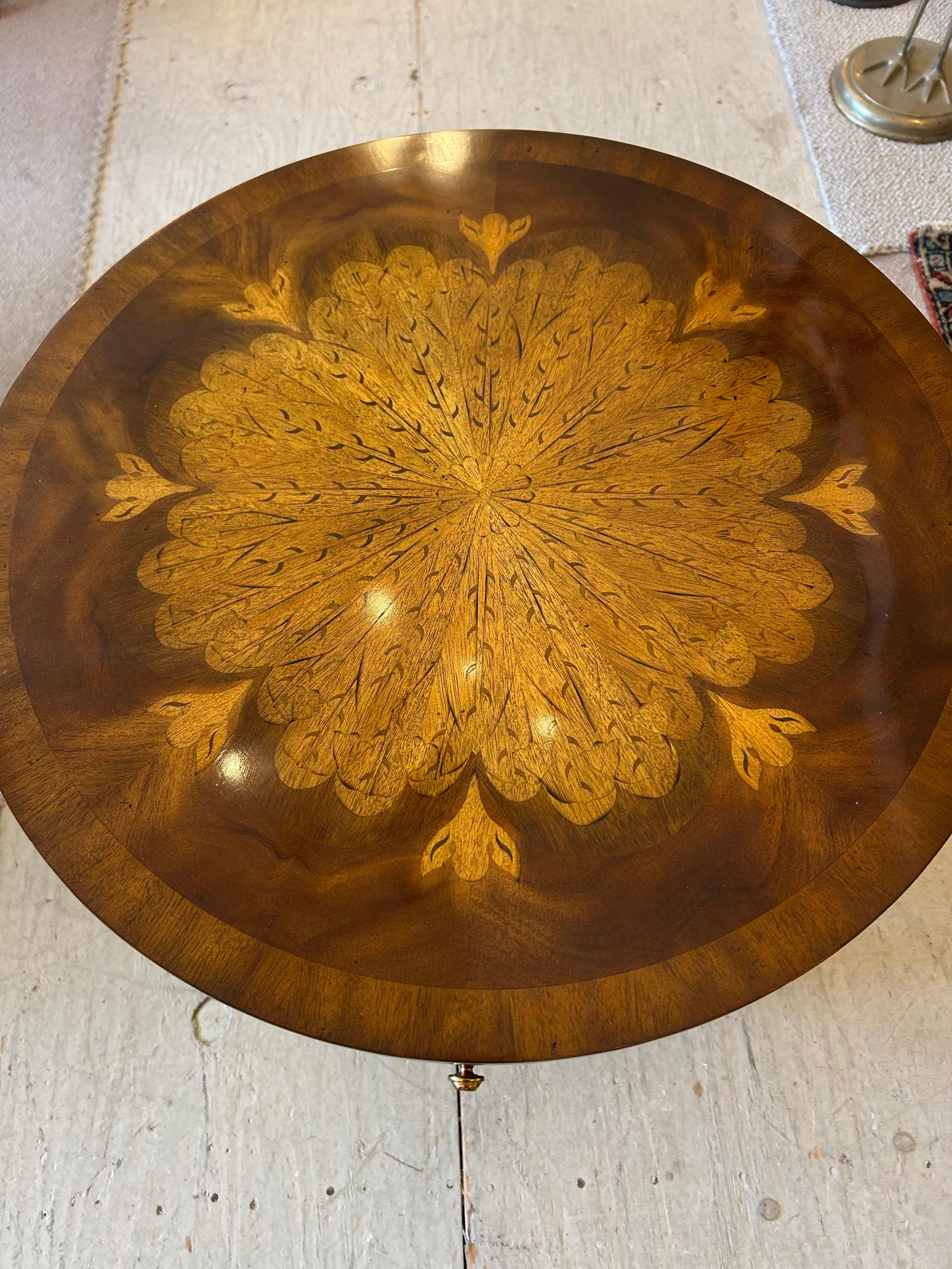 Elegante tavolino rotondo di Maitland Smith, realizzato con un mix di legni, intarsiato con uno splendido motivo floreale decorativo e con pomelli in finitura bronzo, cassetto singolo e piano inferiore.

TS