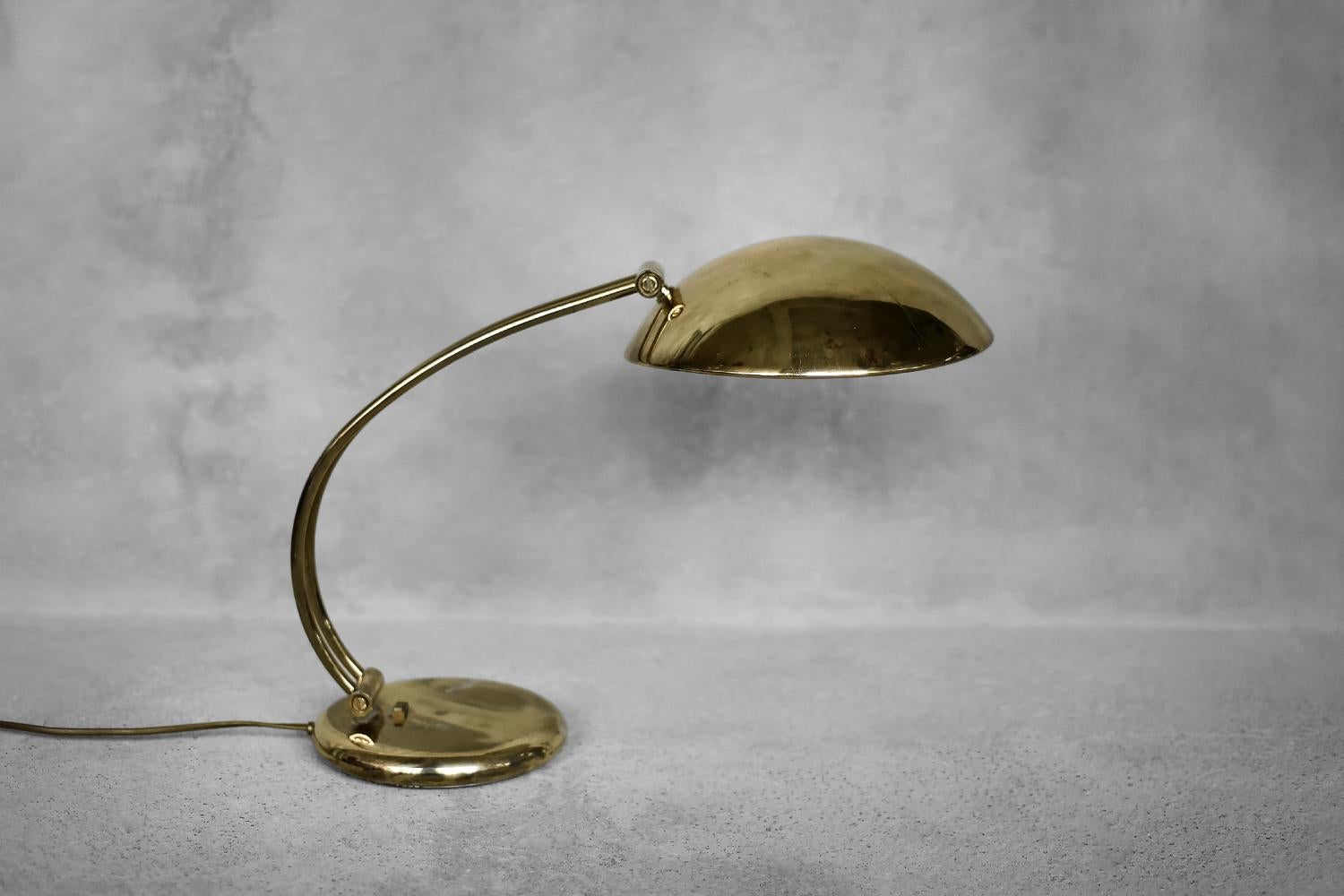 This elegant, gold desk lamp was produced by the Belgian manufacturer Massive during the 1970s. The round base is combined with a large, cylindrical lampshade attached to an articulated arm. The arm and shade can be adjusted to obtain a wide angle
