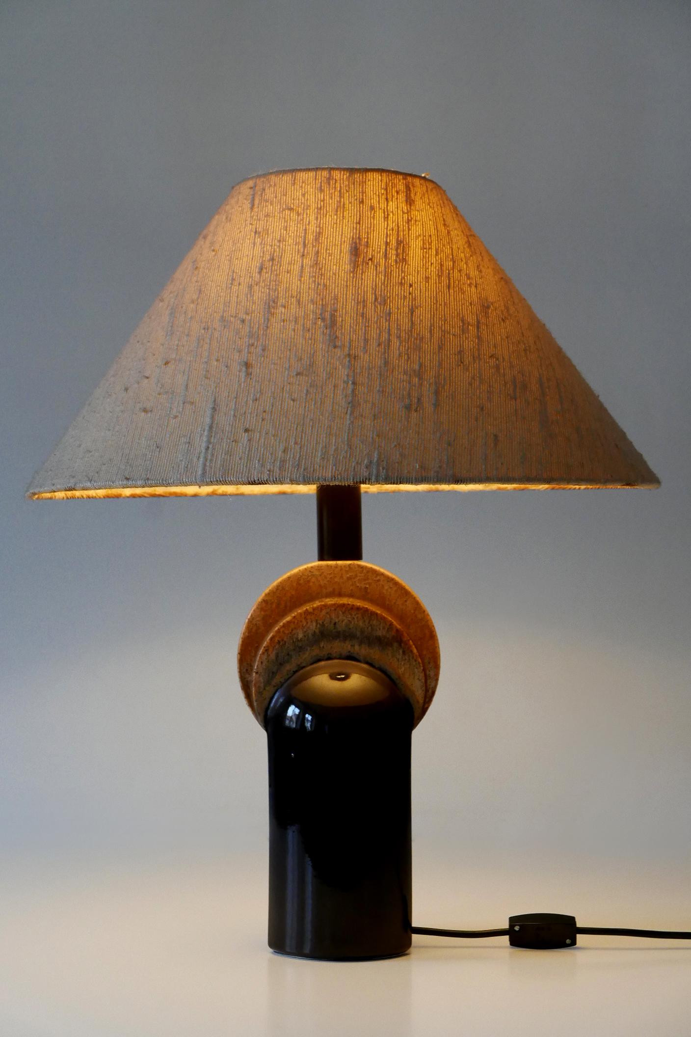 Äußerst seltene und elegante Keramik-Tischlampe aus der Jahrhundertmitte. Entworfen und hergestellt von Leola Design, Deutschland, 1960er Jahre. Etikett des Herstellers auf dem Sockel.

Die aus Keramik und Stoff gefertigte Tischleuchte wird mit 1 x