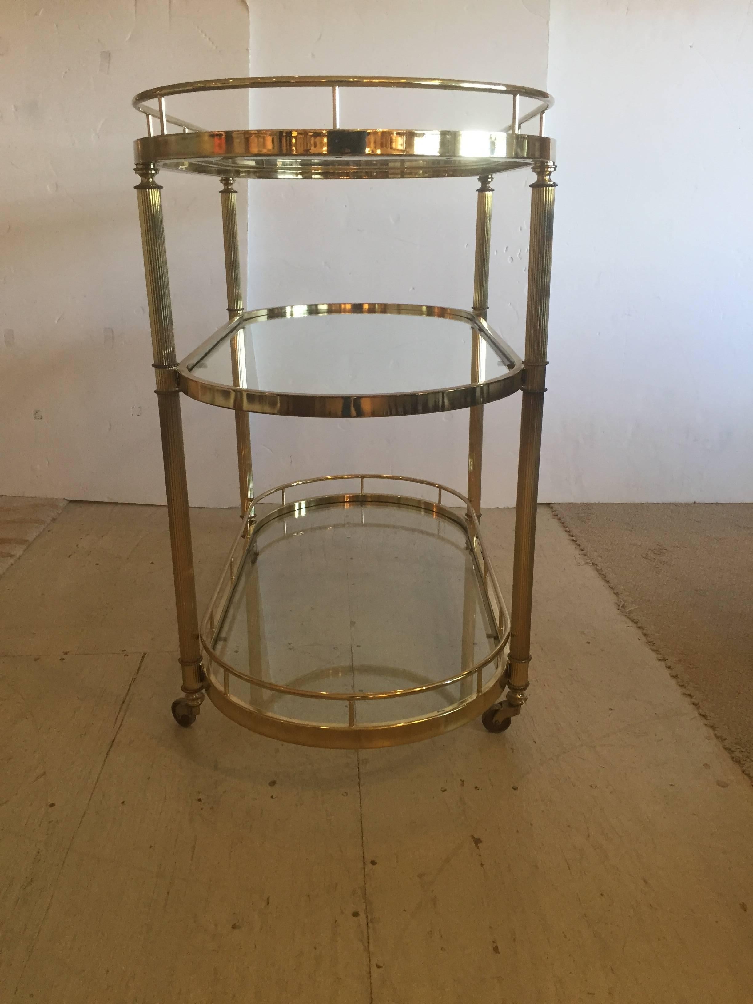 Stately Mid-Century Modern fluted brass bar cart on casters with three oval glass shelves.