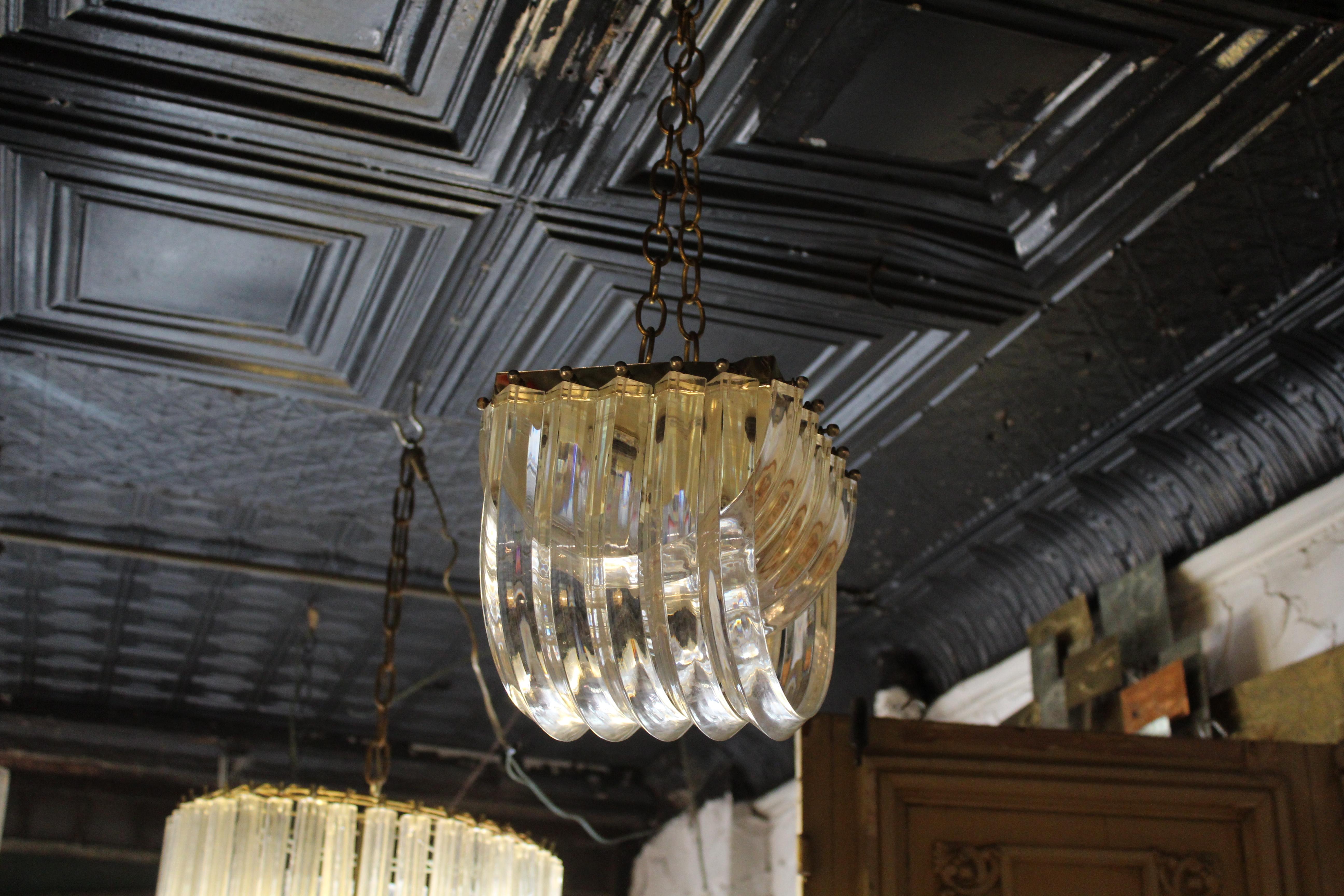 Lampadario moderno di metà secolo realizzato in lucite, con un design scultoreo che cattura e riflette la luce con eleganza. La sua forma audace e la sua struttura trasparente le conferiscono presenza e versatilità, rendendola un pezzo forte per gli
