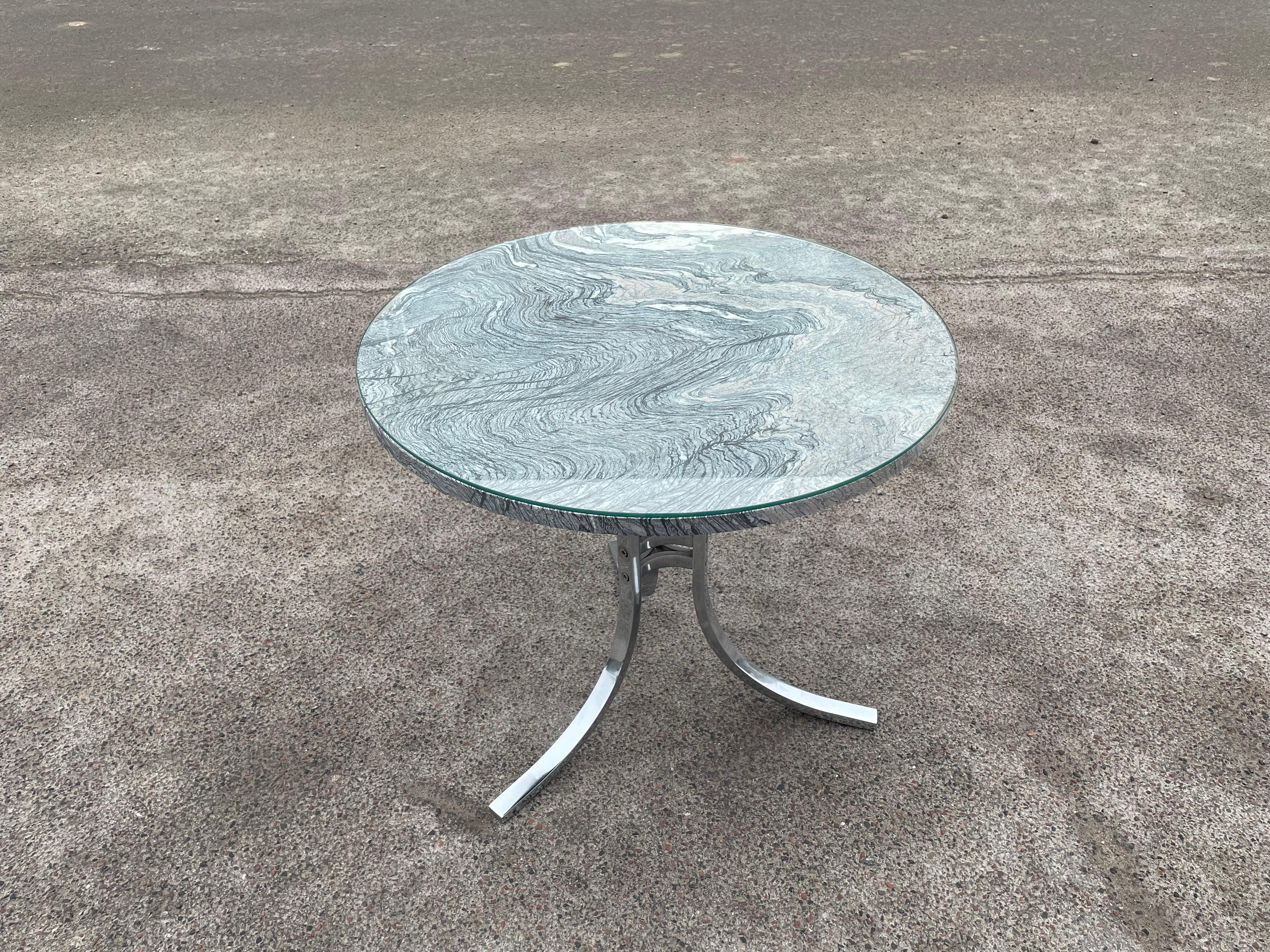 Cette table d'appoint vintage moderne est dotée d'un plateau rond en marbre surmonté d'un verre et d'une élégante base chromée.